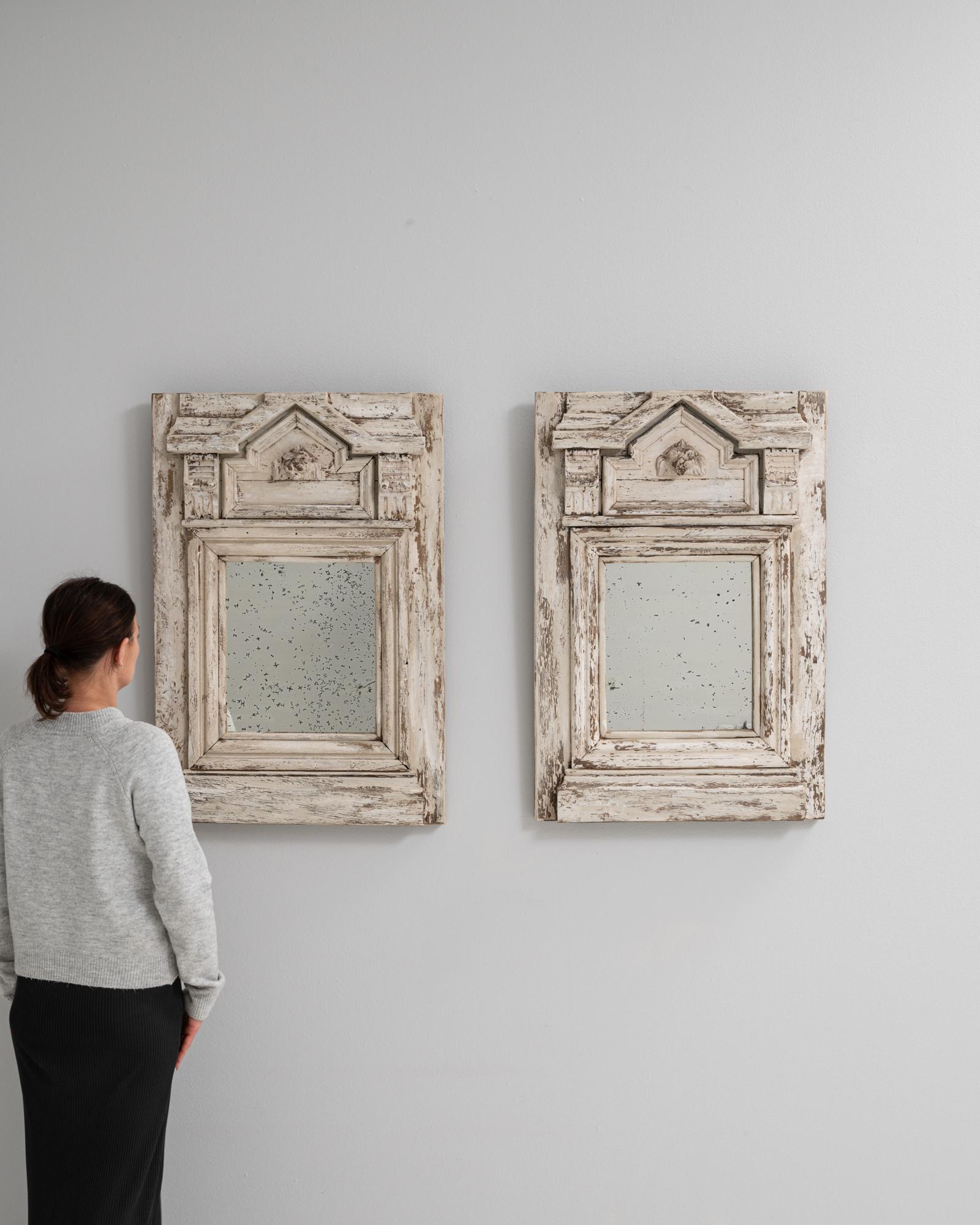 Cette paire de miroirs français du XIXe siècle présente des cadres en bois à l'architecture audacieuse avec une finition patinée blanche, magnifiquement altérée par le temps. Les couronnes des frontons triangulaires sont ornées de têtes de lion