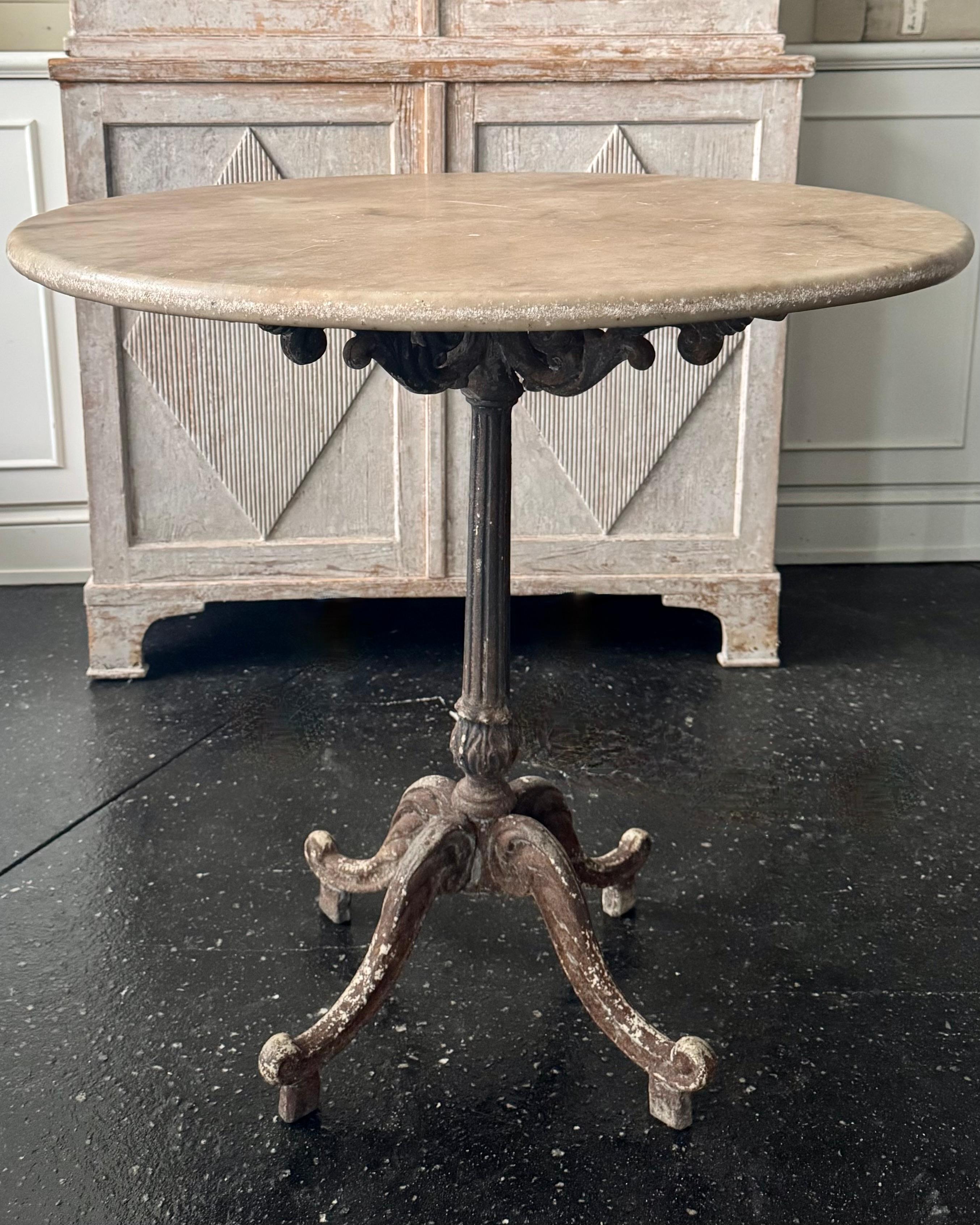 Elégante table de bistrot parisienne française de la fin du 19ème siècle avec un épais plateau en marbre blanc patiné. La base en fonte solide, richement ornementée, avec quatre pieds à volutes et patinée par le temps, ajoute une touche d'histoire.