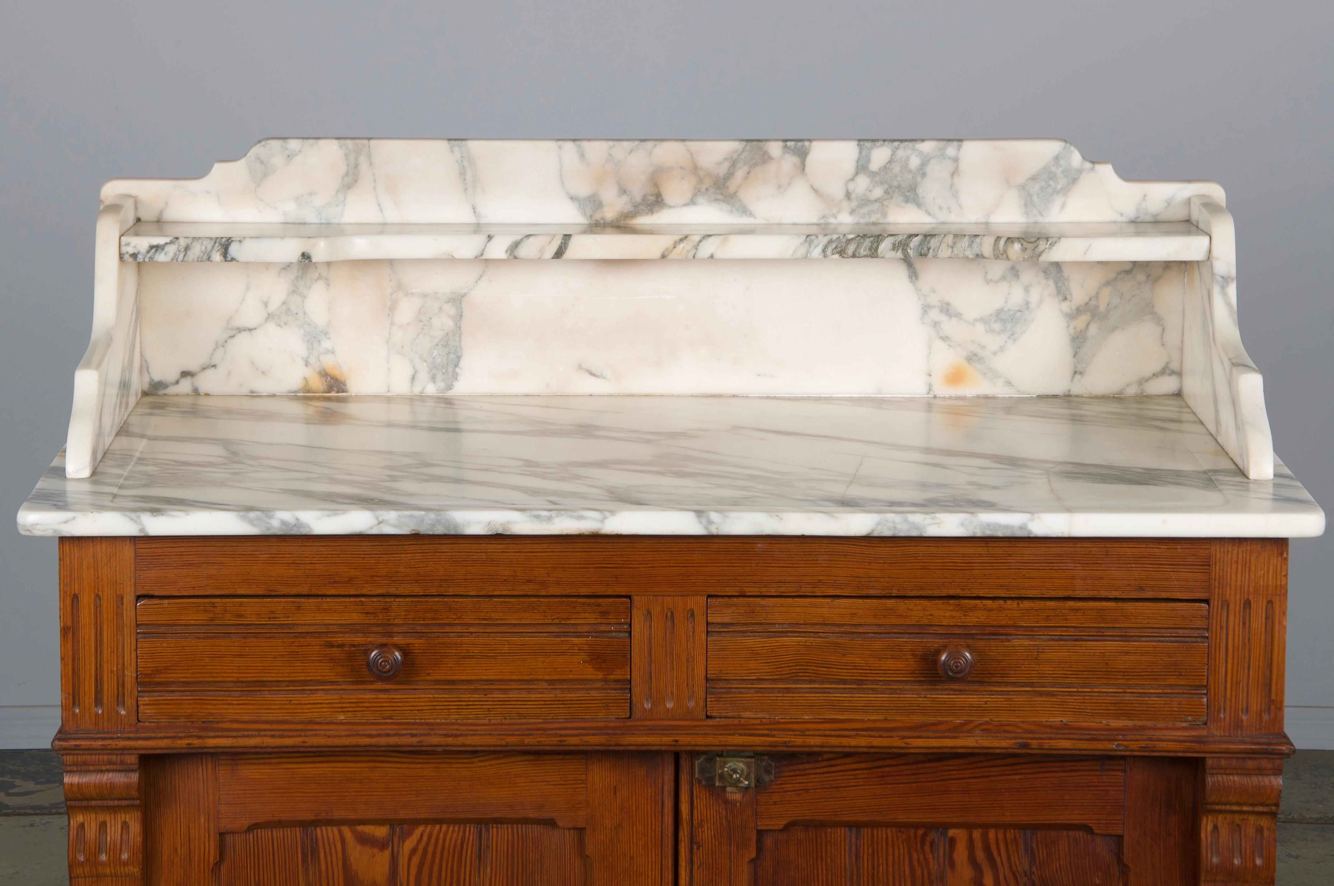 An exquisite late 19th-century French Parisian washstand or vanity, sourced from Provence, France. This piece features a rustic pine storage cabinet topped with stunning Calacatta Viola marble. The marble includes a single shelf and showcases a