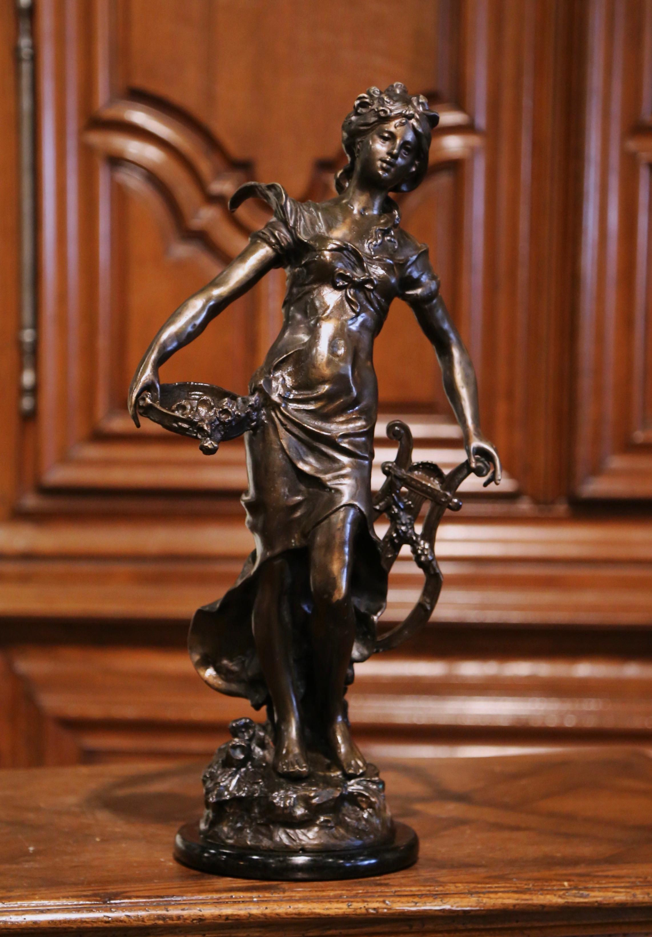 Created in France circa 1890, this antique bronze sculpture depicts a young and elegant beauty holding a lyre in one hand, and a basket of grapes in the other. The female figure stands on a round black base. The allegorical Art Nouveau work is