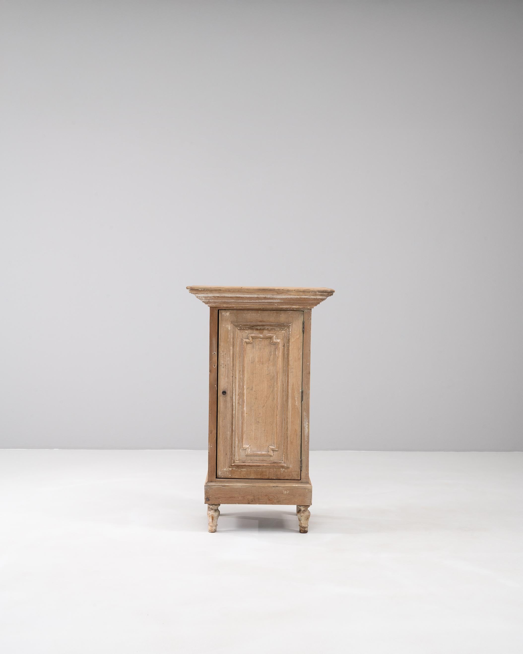 Questo mobile francese patinato del XIX secolo mostra il fascino dell'artigianato di provincia con il suo design sobrio e la sua finitura consumata dal tempo. Realizzato in legno massiccio, l'armadietto presenta un'anta a pannello singolo con