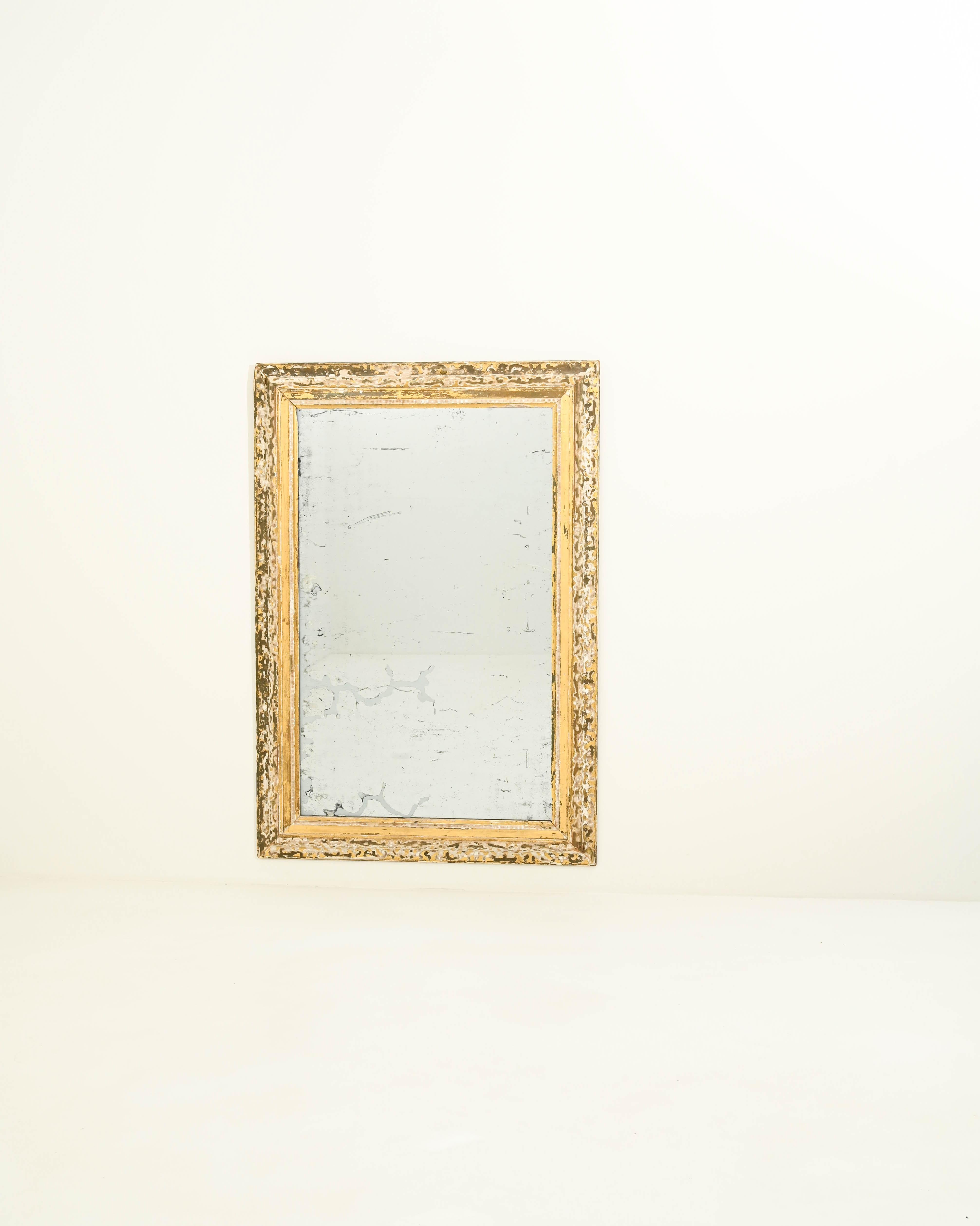 Designed for spacious, opulent rooms, this 19th-century looking glass commands attention with its large-scale presence. The hand-crafted rectangular wooden frame showcases intricate patterns etched by a distressed golden leaf patina. The richly