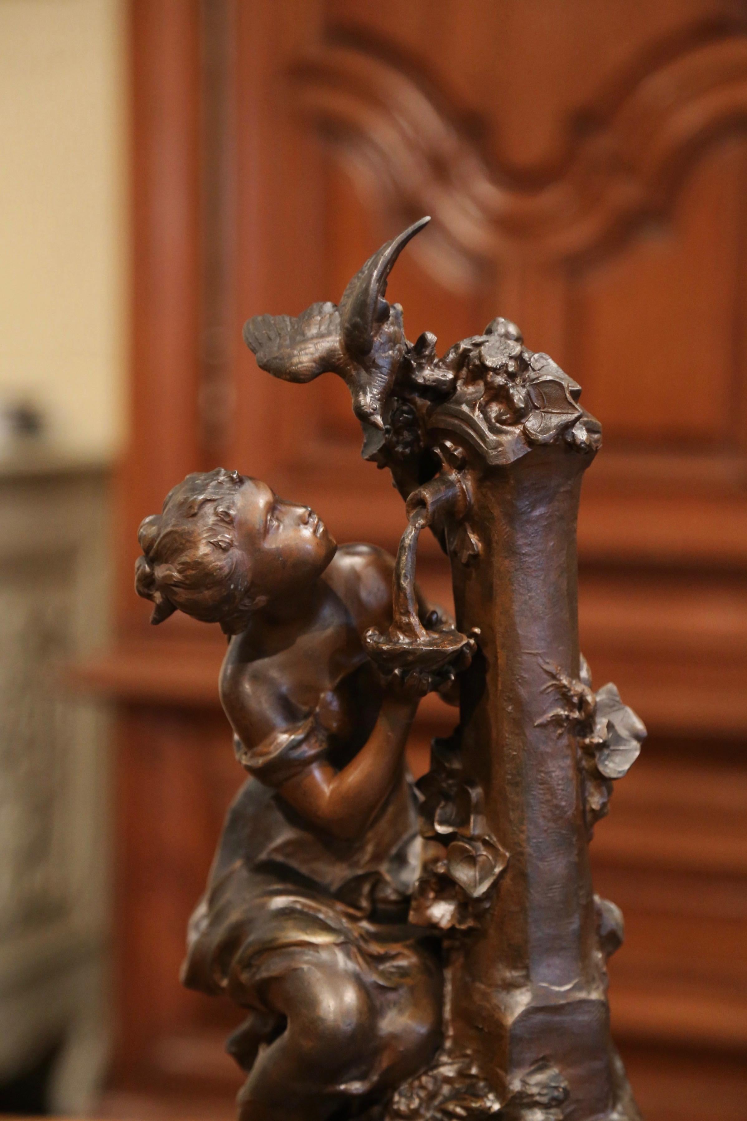 This elegant figure composition was crafted in France circa 1880; made of spelter, the statue depicts a young seated beauty drinking from a watering fountain with bird perched on the top of the cantral pillar. The subject features fine details, and
