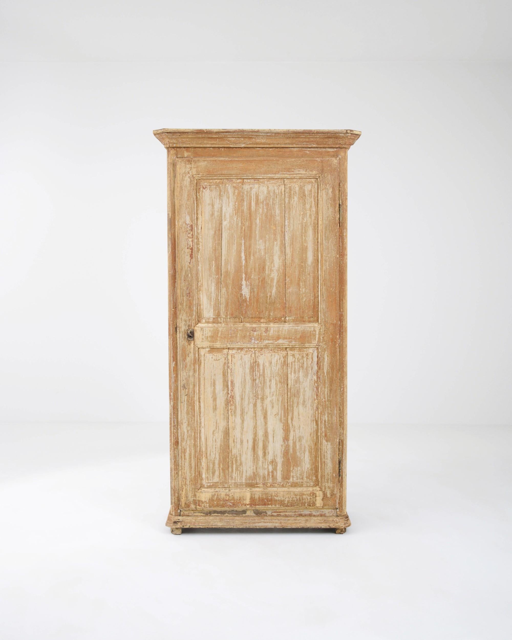 A timeworn patina gives this antique wooden cabinet a unique appeal. Hand-built in France in the 1800s, the once-painted surface of the exterior has worn to a soft craquelure, beneath which the warm tone of the natural wood is visible. The tall door