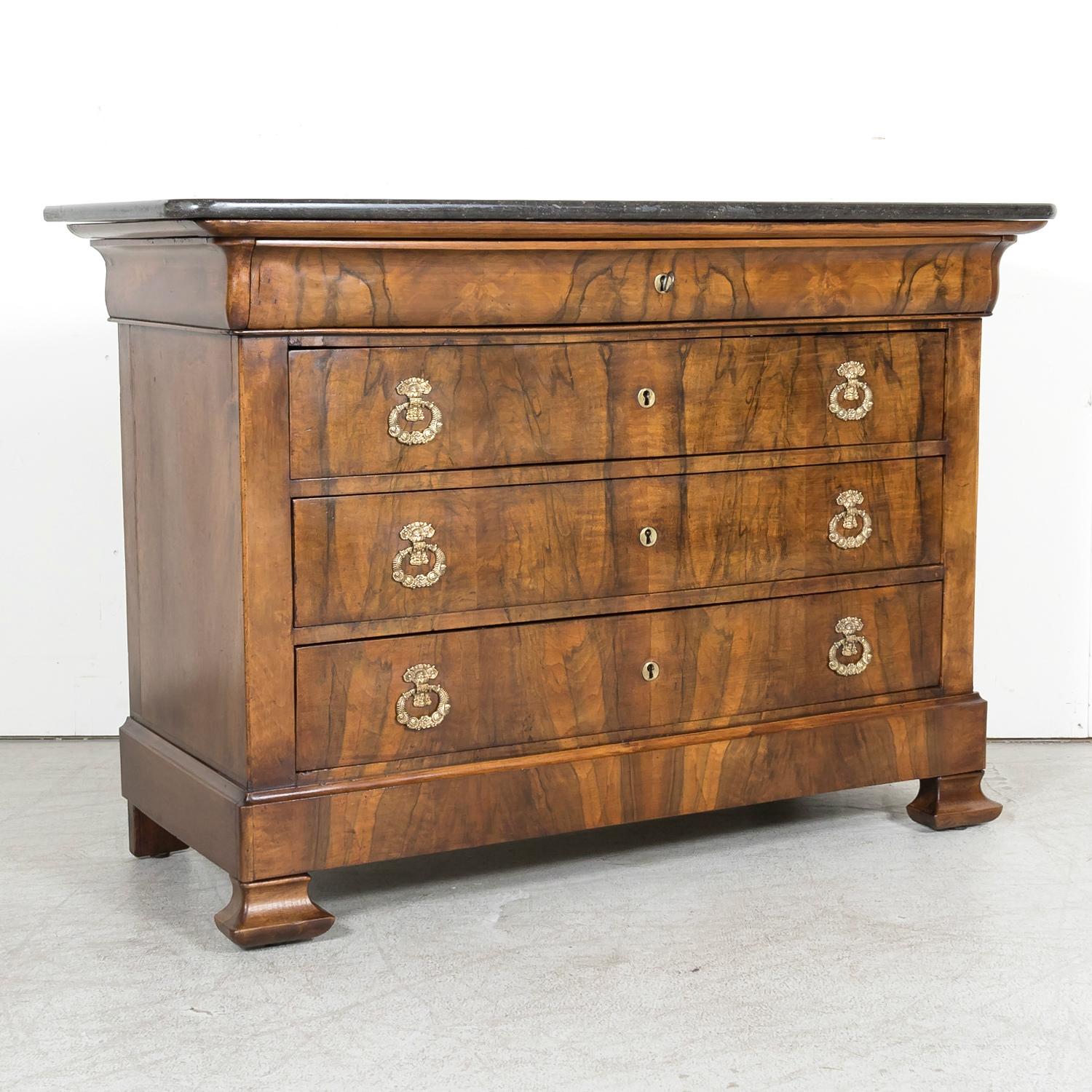 A 19th century French Louis Philippe period four-drawer commode handcrafted by talented artisans in Lyon of walnut and burled walnut, circa 1830s. Having the original black fossil marble top, this handsome antique French chest of drawers features a