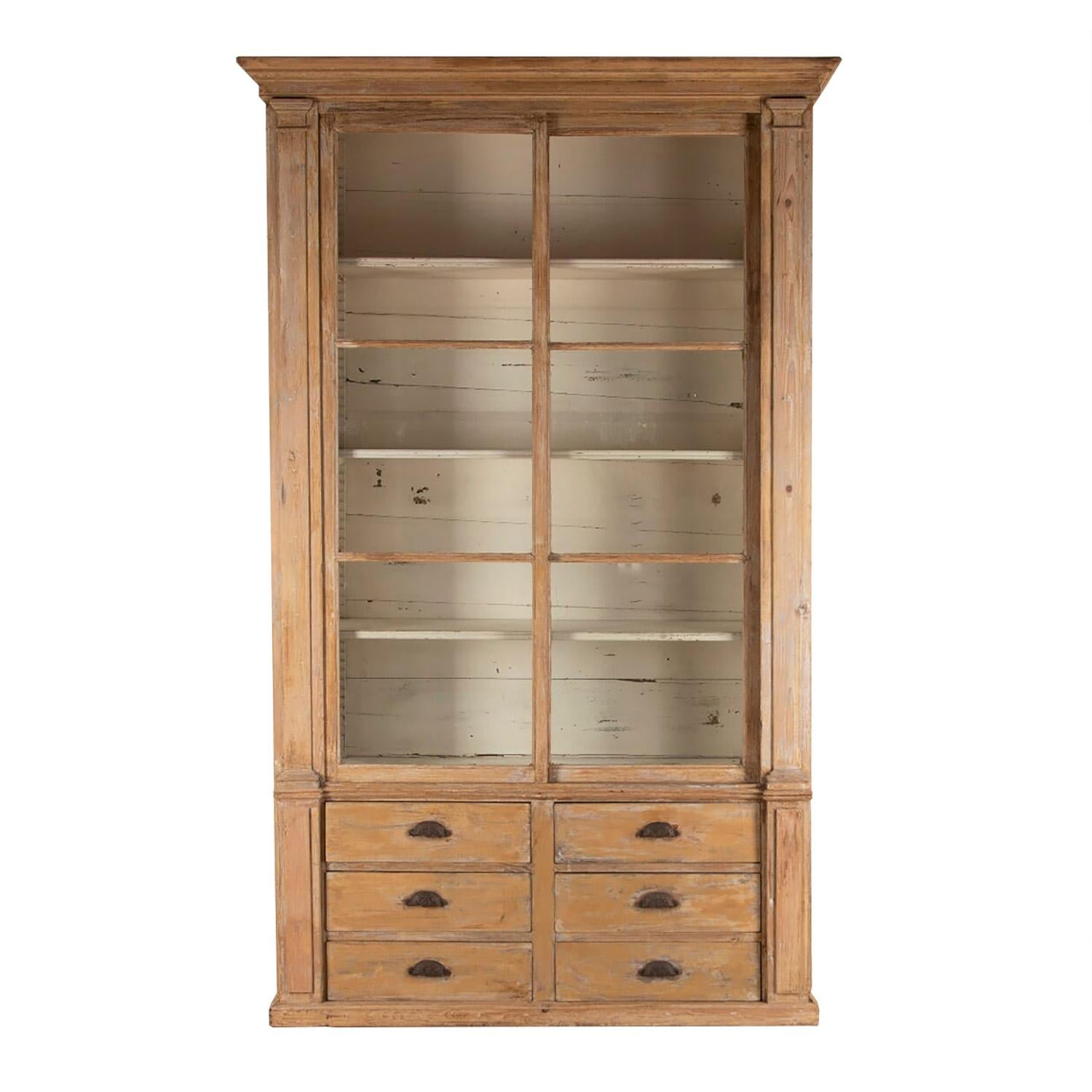 Early 19th century pharmacy cabinet with original paint. This piece has a glass sliding door which opens to shelved storage, below are six useful drawers with original handles.