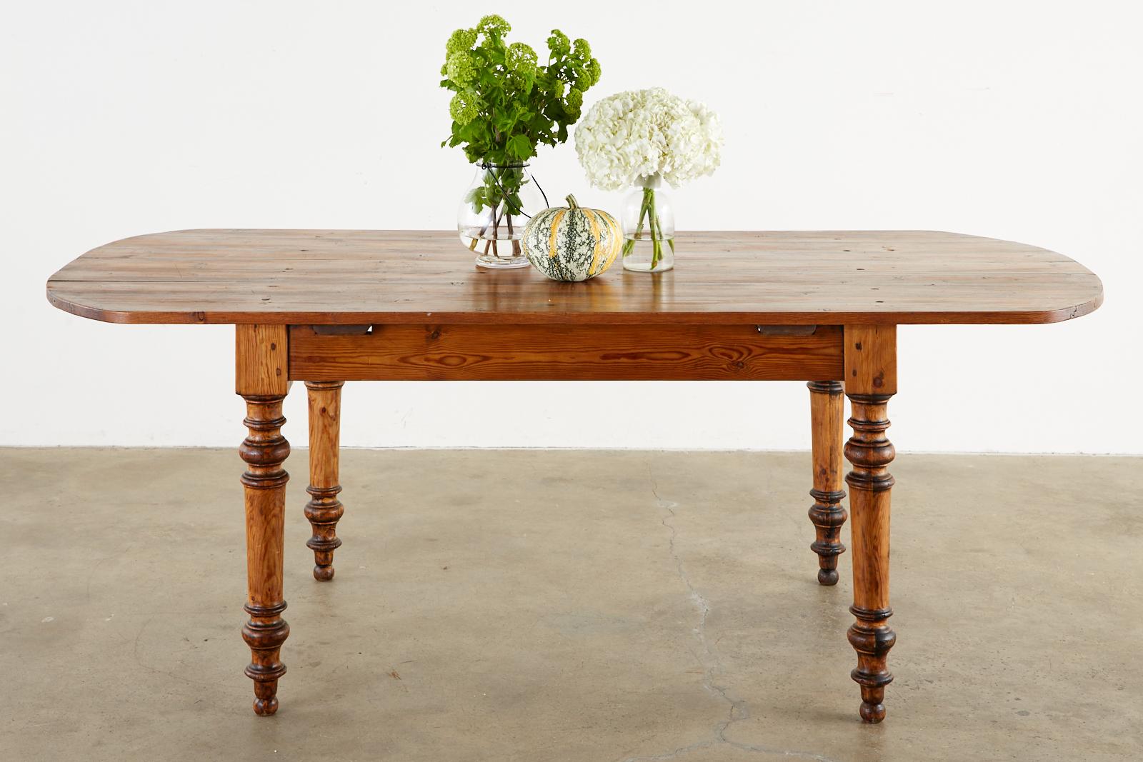 Rustic 19th century country French farmhouse harvest table or dining table. Hand-crafted from pine planks on the top with tongue and groove joinery having rounded ends. The thick, turned legs have wood peg joinery. The pine has a lovely aged patina