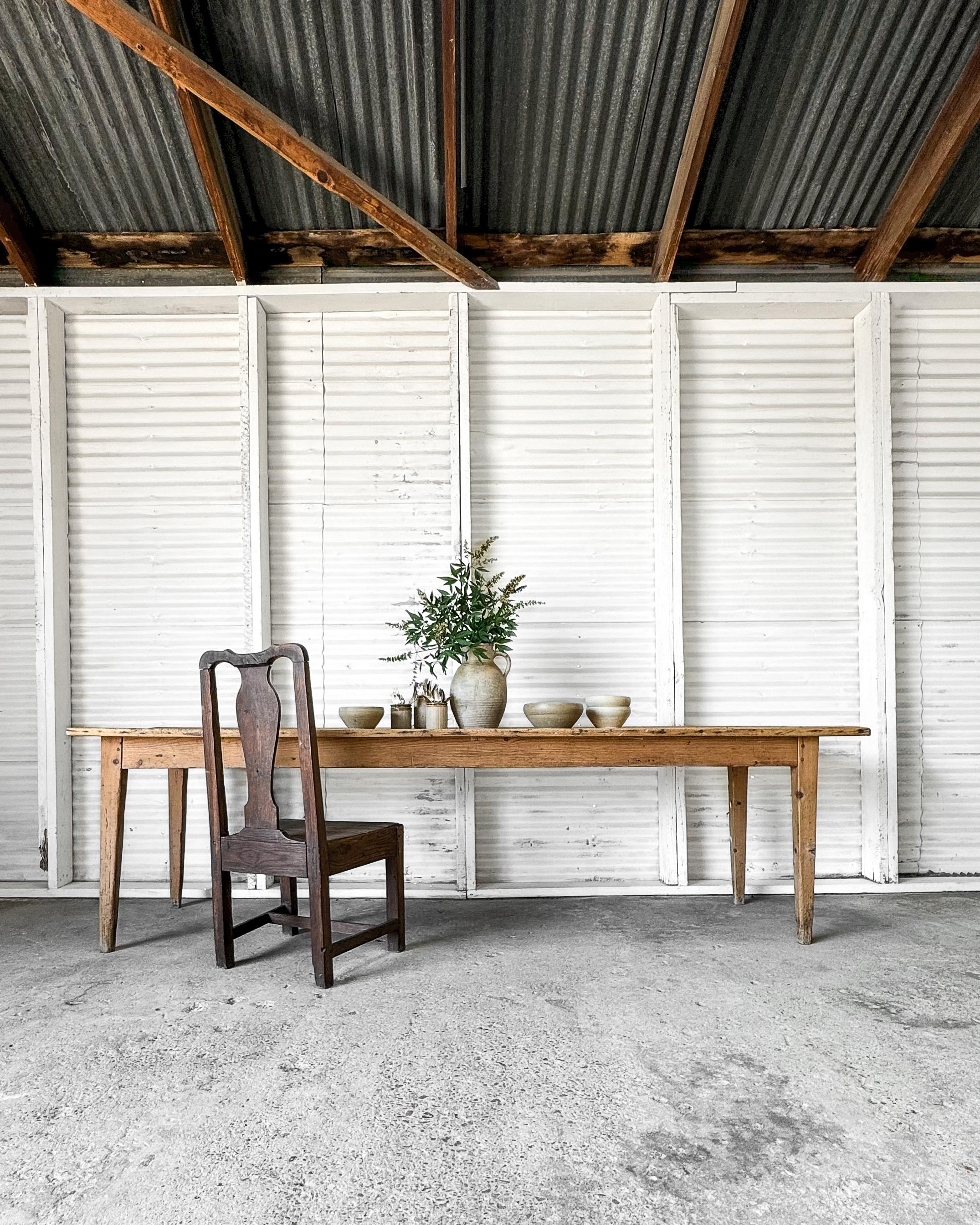 An antique French harvest dining table that embodies the rustic charm and craftsmanship of traditional country farmhouse furniture. Handcrafted from pine, the table features narrow tapered legs that provide both stability and refined simplicity. The