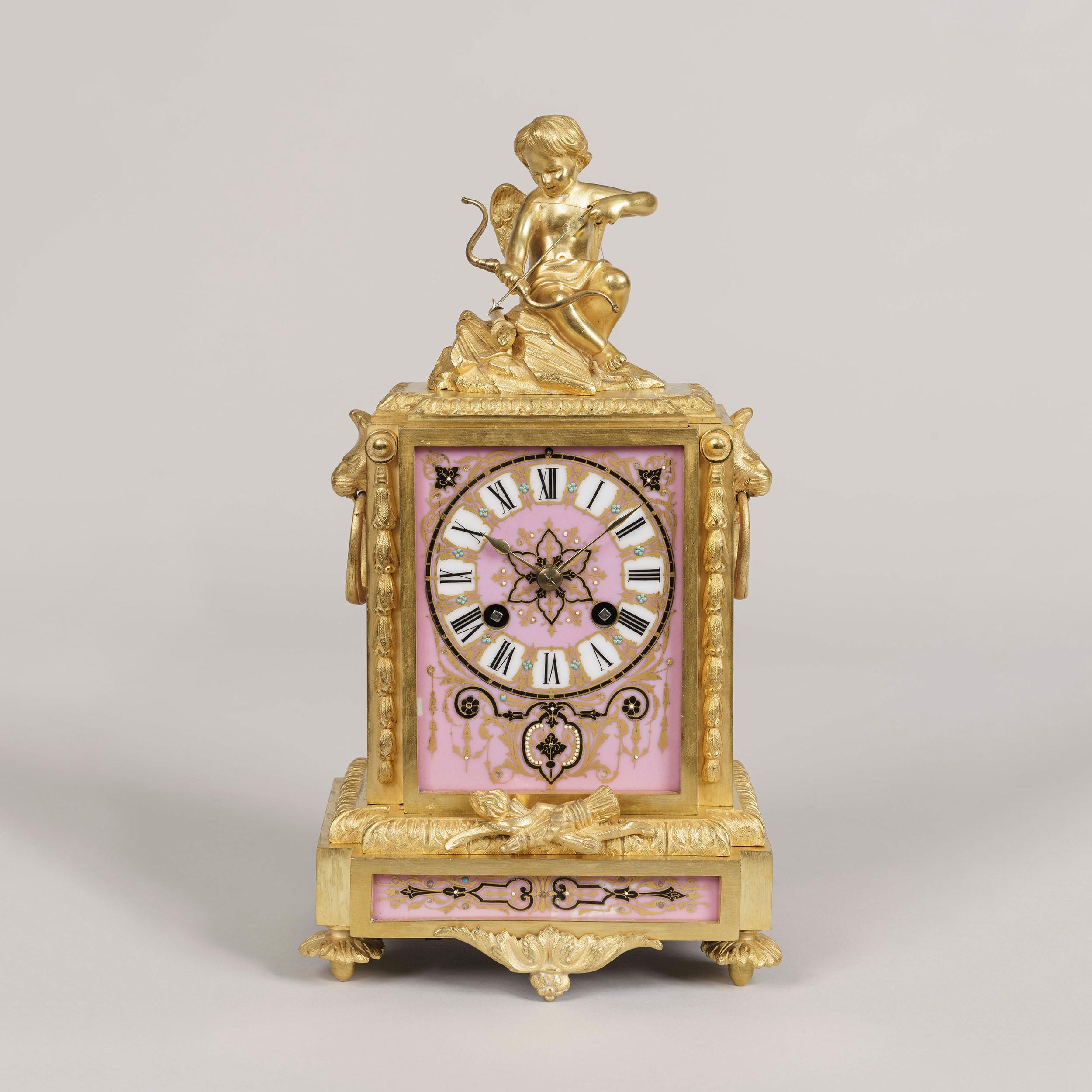 Une horloge symbolique de style Louis XVI
Par Japy Fréres et Cie.

Le boîtier en bronze doré finement ciselé englobe des panneaux de porcelaine rose décorés de perles sur la face et les côtés, le tout surmonté de la figure de Cupidon et de son
