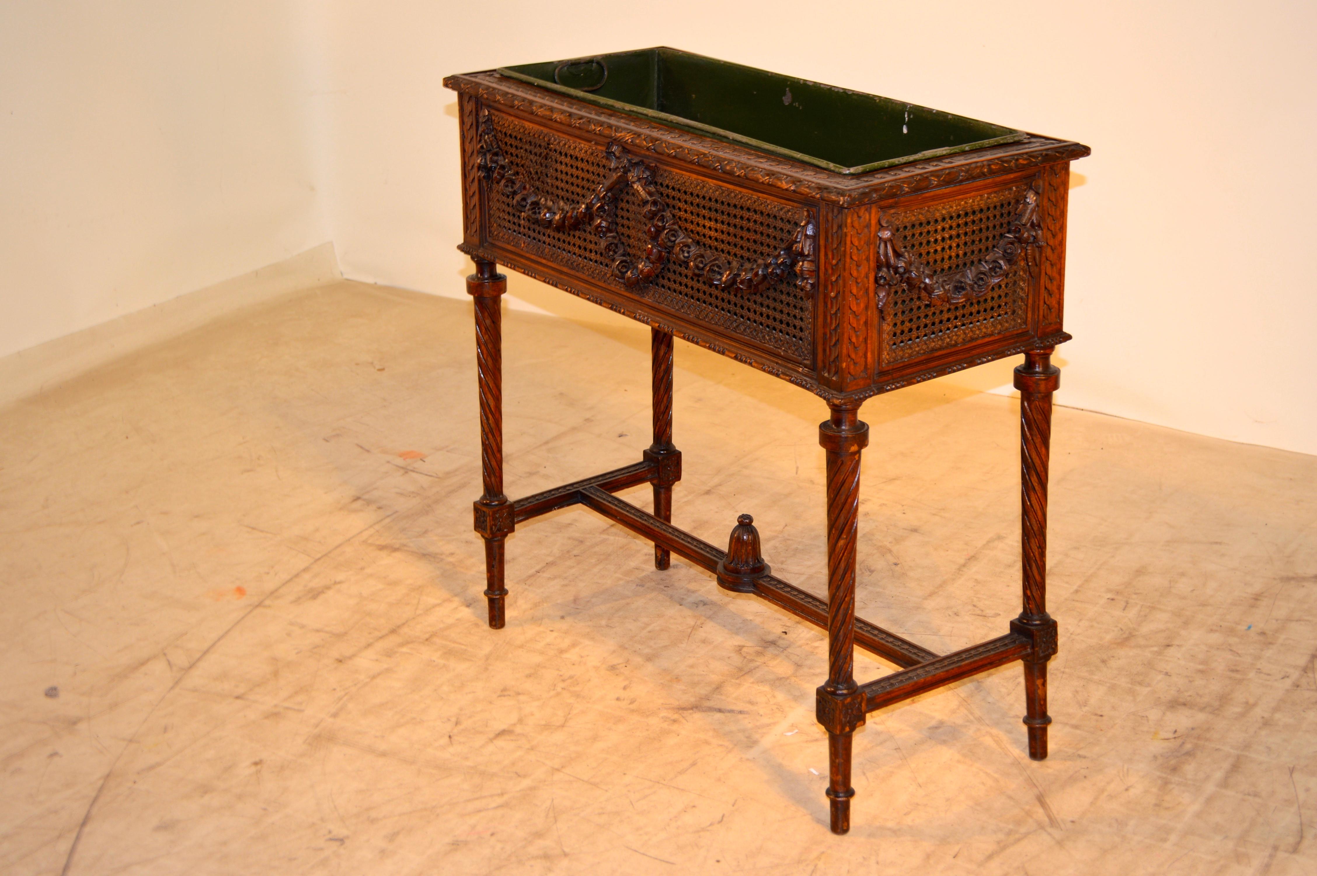 19th century French planter on stand with three caned sides with applied carving floral swags joined by a wreath on the front. The back has been newly upholstered in linen. Wonderfully carved legs and frame. The liner has signs of wear and losses