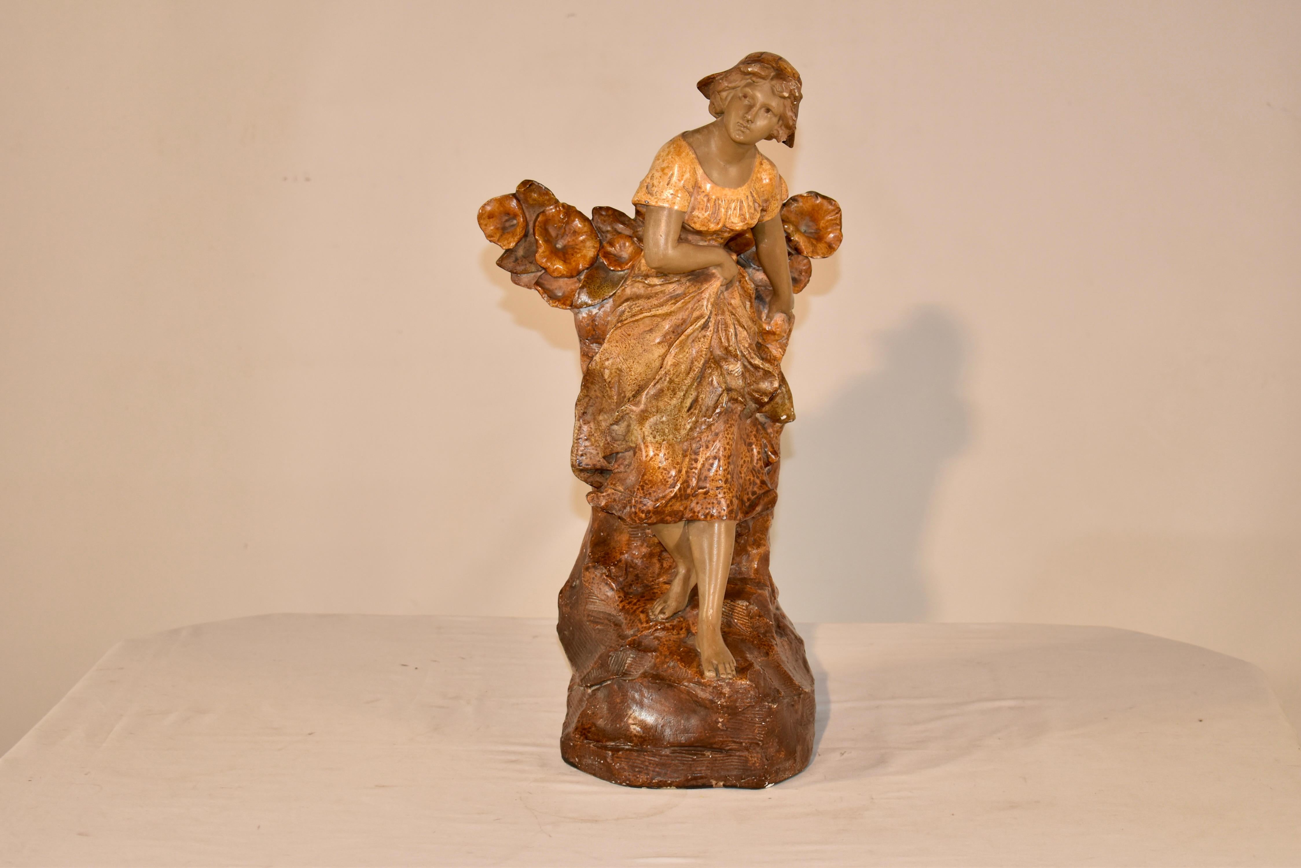 Figura in gesso art nouveau del XIX secolo di una donna a piedi nudi che sorregge il suo vestito e attraversa un terreno roccioso.  Indossa un bel cappello ed è circondata da uno swag floreale.  Il pezzo è firmato sul retro.  