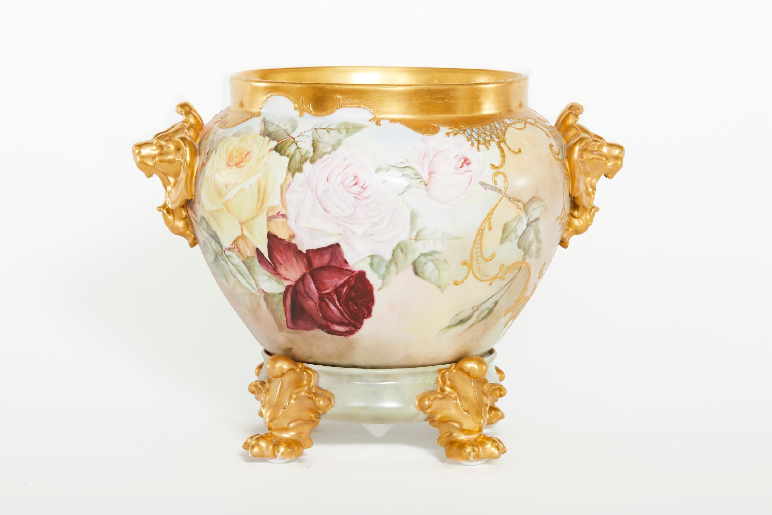 Beautiful and elegant french porcelain two piece cachepot / jardiniere with exterior hand painted floral design details. The jardiniere / cachepot features a detachable footed holding base and gilt top design side handles. The cachepot is in good