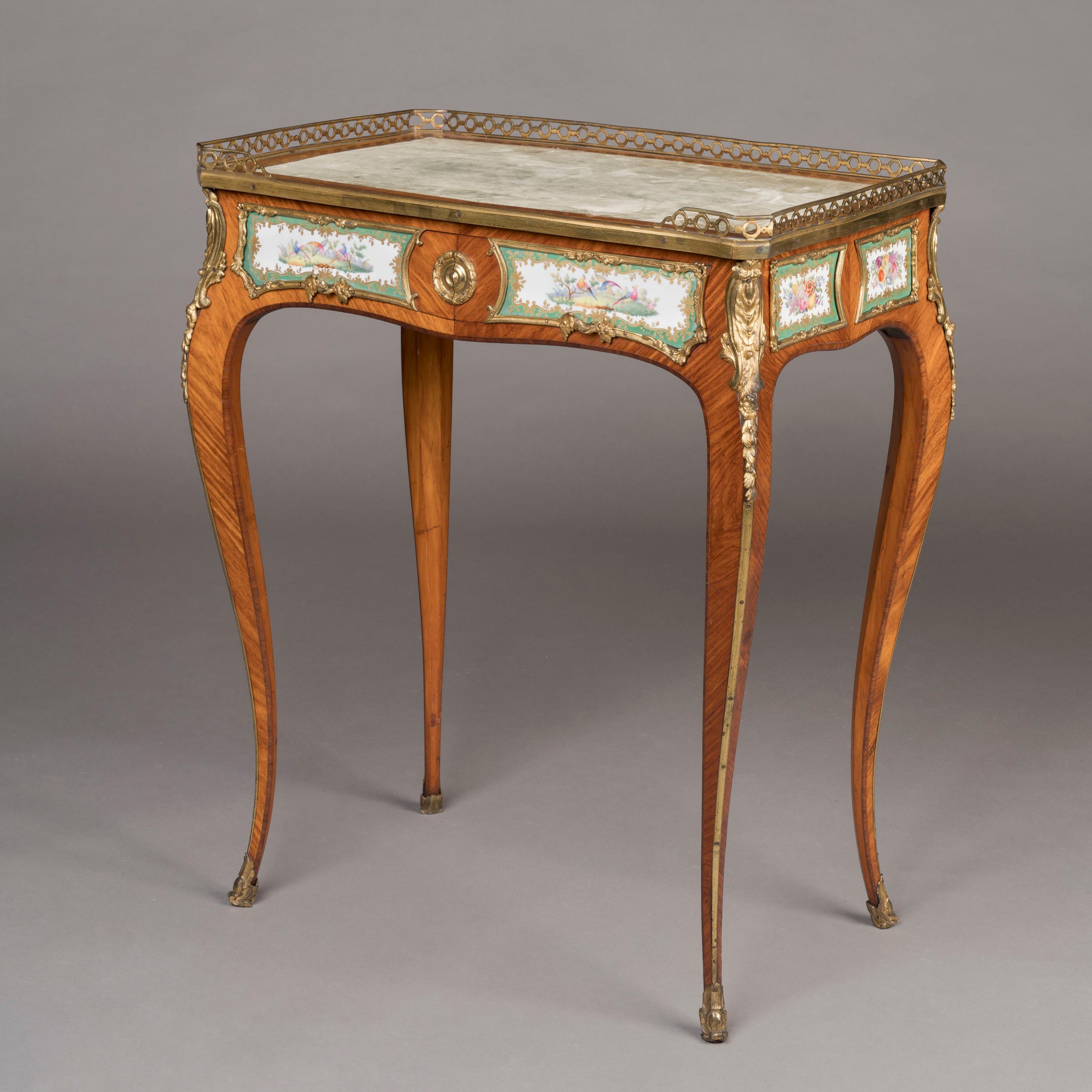 A Porcelain-Mounted Occasional Table in the Transitional Manner
Attributed to Edward Holmes Baldock

Constructed from kingwood and tulipwood, with ormolu mounts in the Louis XV/XVI transitional style, supported on cabriole lefs with sabot feet, the