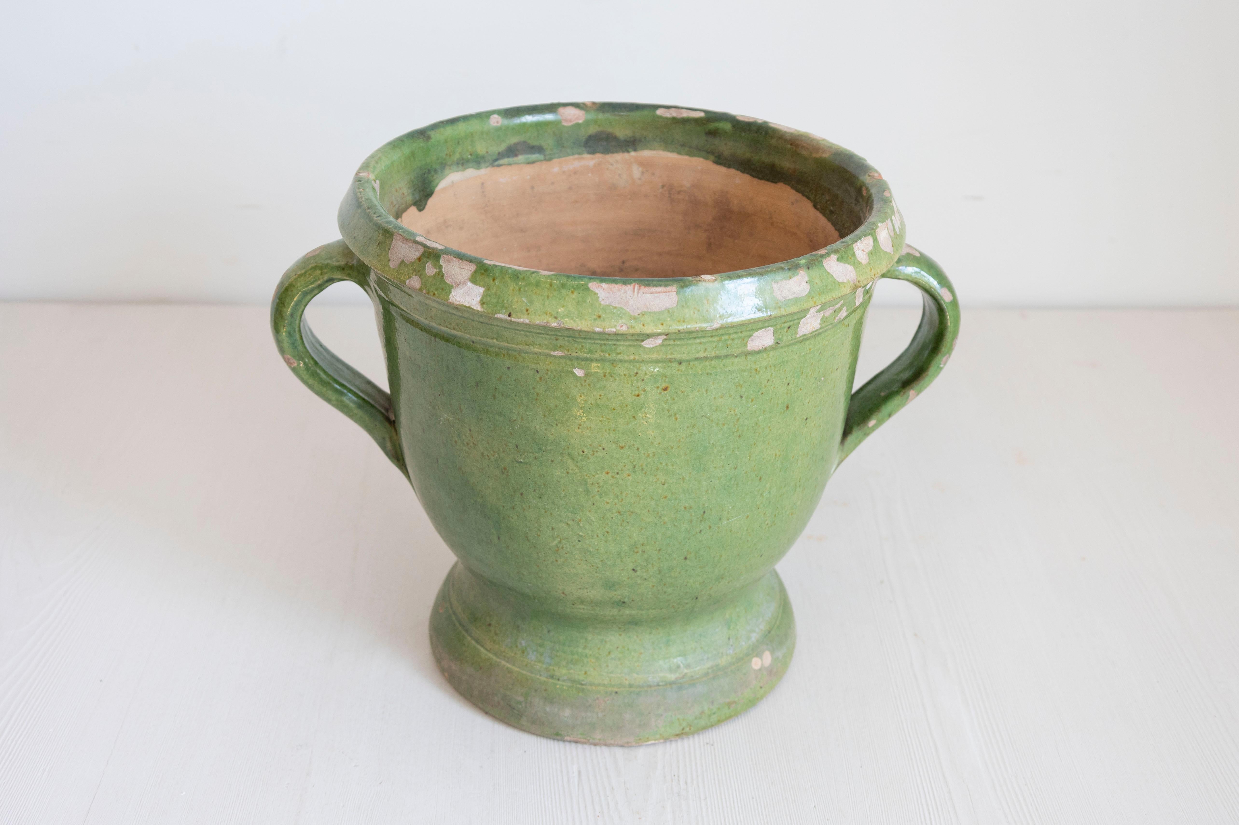 Cette jardinière en poterie française du XIXe siècle, avec sa belle glaçure verte, illustre l'élégance rustique classique. La pièce a une forme d'urne avec deux poignées gracieusement incurvées de chaque côté. La glaçure verte s'est altérée au fil