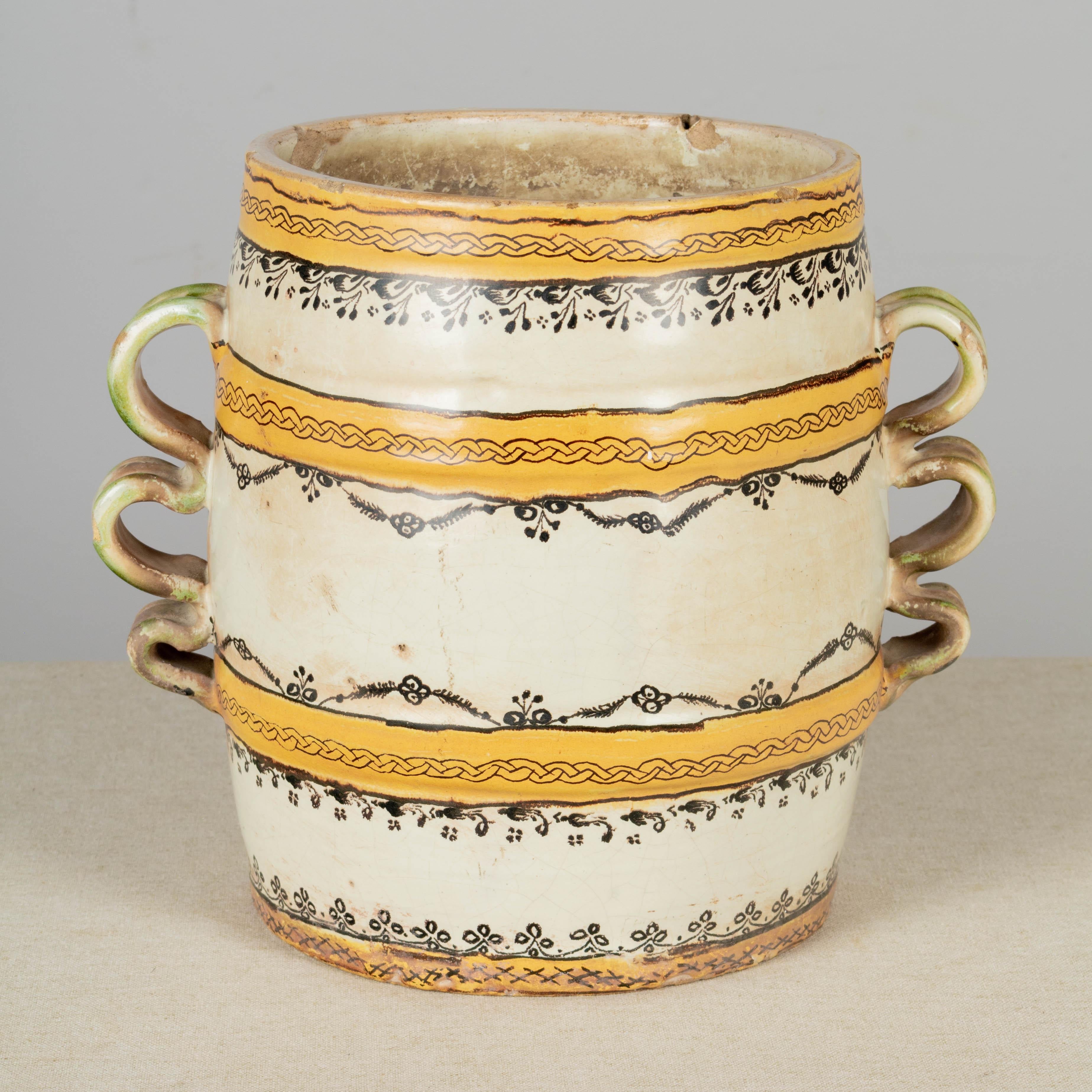 An early 19th Century white glazed terracotta earthenware pottery jar from the East of France. Decorated with yellow bands with black painted details and pale green glazed triple loop handles. Drainage hole in bottom. Rustic condition with several