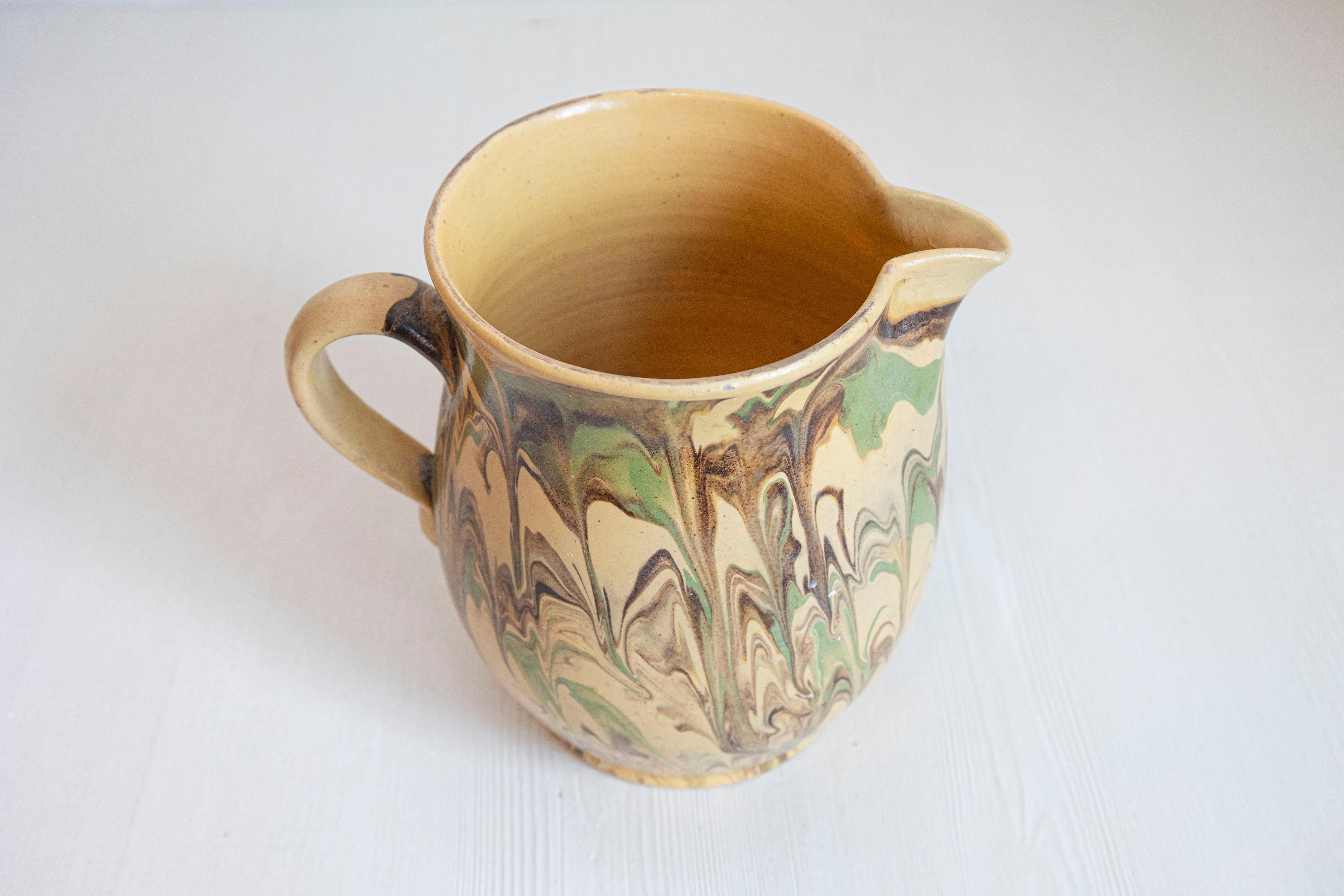 A French pottery pitcher from the 19th century, with green and brown marble style design. Created in France during the 19th century, this pottery pitcher features a yellow ground accented with a lovely dripping décor and green and brown tones