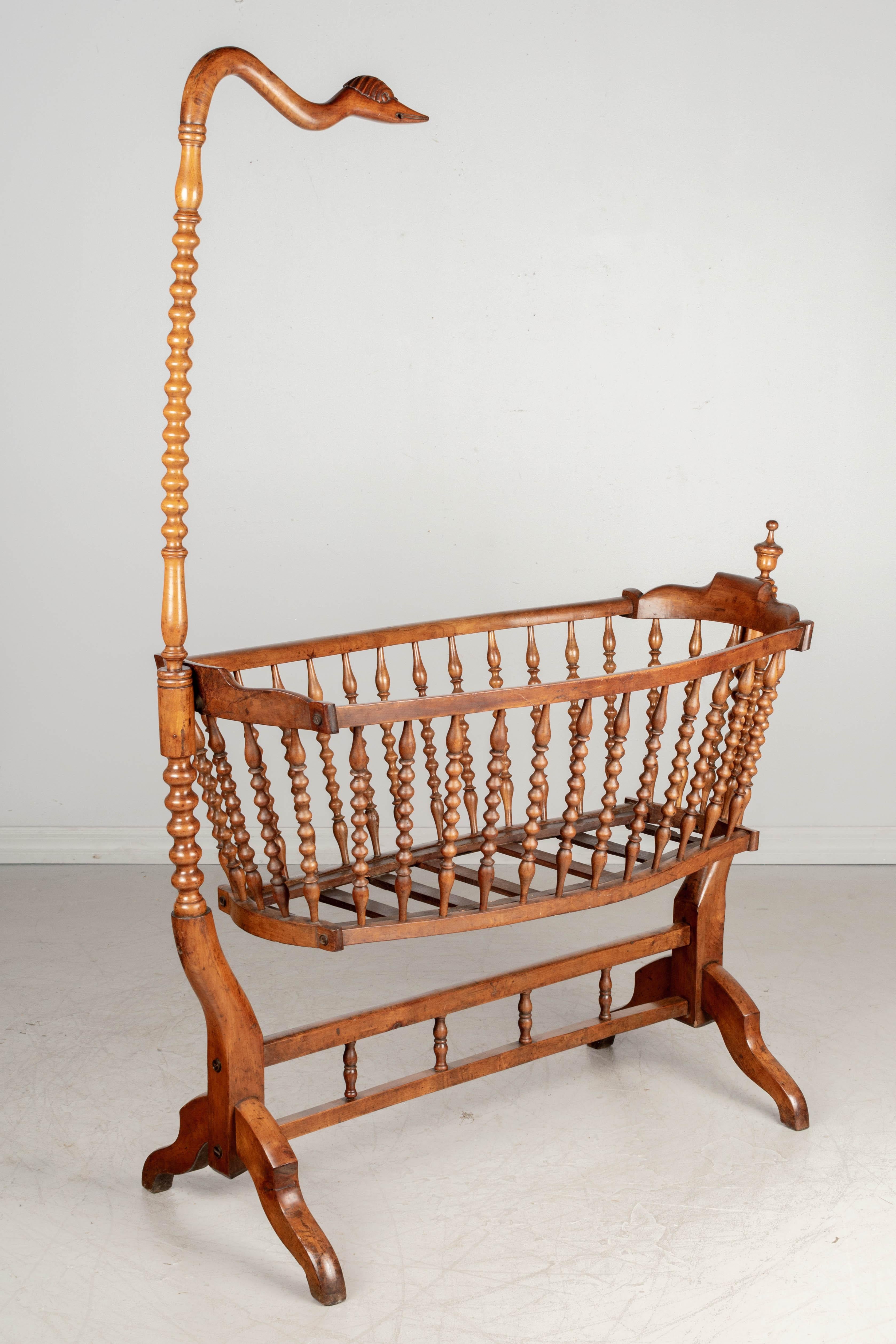 A 19th century French baby cradle from the Provence region made of mahogany with nicely turned spindle rails. Fitted with a tall pole with a carved swan head that was used to attach a fabric netting. The cradle gently rocks on the sturdy frame.