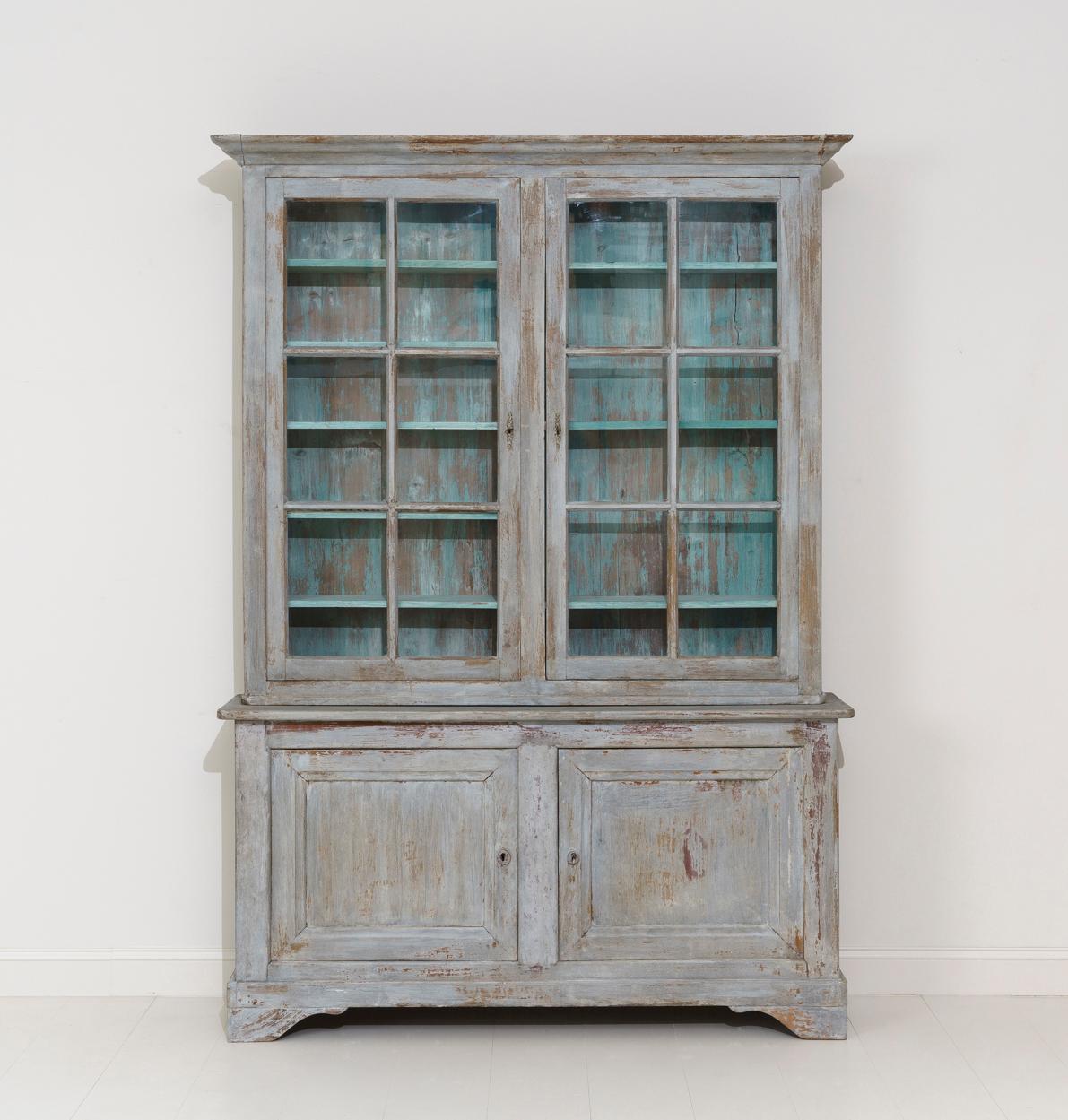 A beautiful French two-part painted library or bookcase in the Louis Philippe style with original glass from the Provence region of France. The exterior color of this buffet deux corps is blue - gray and the interior a French blue. The upper cabinet