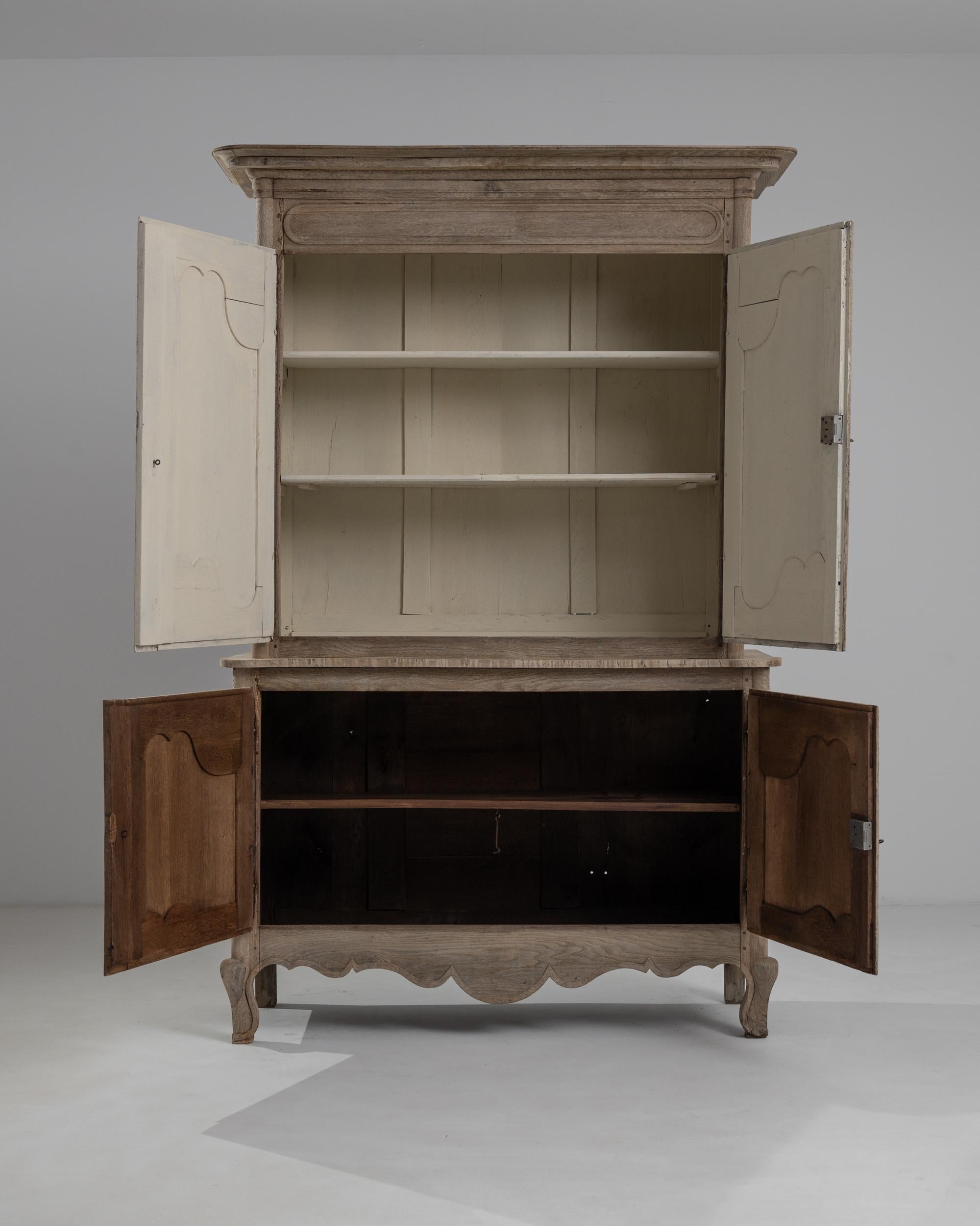 The ashen hue of the bleached oak accentuates the grandeur of this vintage buffet ‘a deux corps’ handcrafted in France circa 1850. Crowned with a molded cornice, this chest boasts deep curvilinear carvings of the panel doors echoed in the waves of