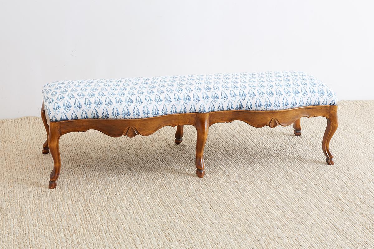 Rustic 19th century French provincial carved walnut bench with a newly upholstered linen seat. Features a hand-carved frame with a serpentine front and scalloped aprons. The seat fits snuggly in the perfectly framed base and is supported by cabriole