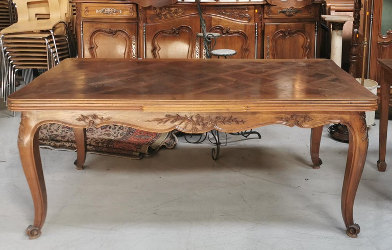 This especially beautiful French provincial dining table in the style of Louis XV is made of walnut with an undulating parquetry inlaid top with drawer extensions that pull-out from both sides to extend the table's surface. It has an undulating