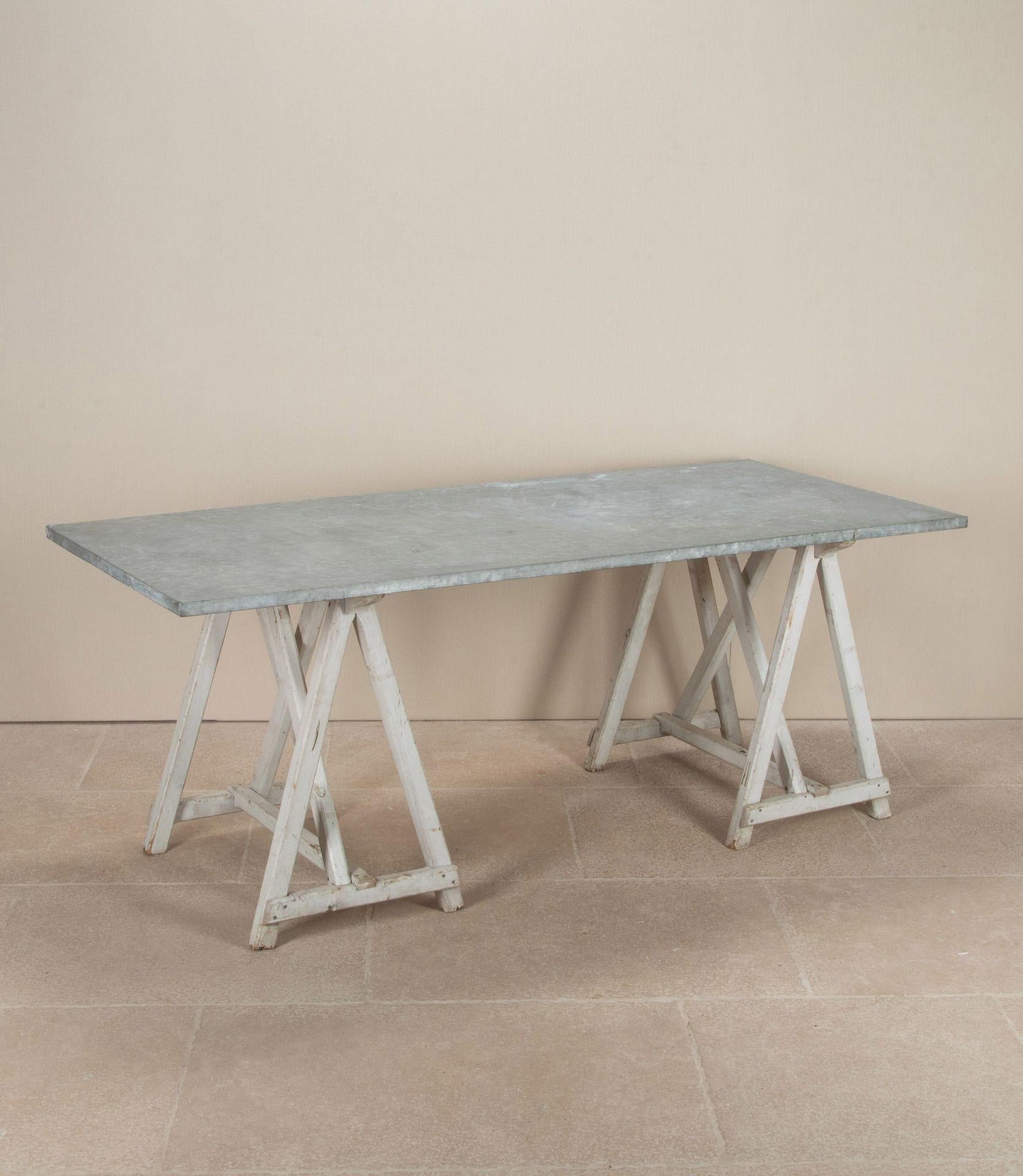 French Provincial 'fleuristes' table with a patinated zinc top. The base comprises two charming 19th Century trestles which have their original paint. A very sturdy table which could be used inside or outside. Easily folded away when not in use.