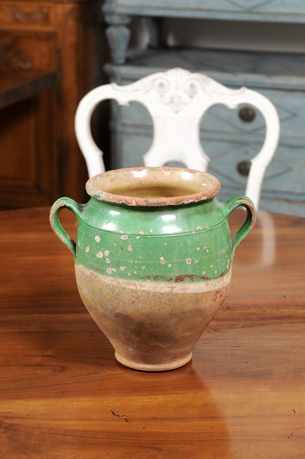 A French green glazed pottery confit pot from the 19th century with two handles and unglazed base. Created in France during the 19th century, this confit pot features a green glaze in its upper section sitting above an unfinished base. Traditionally