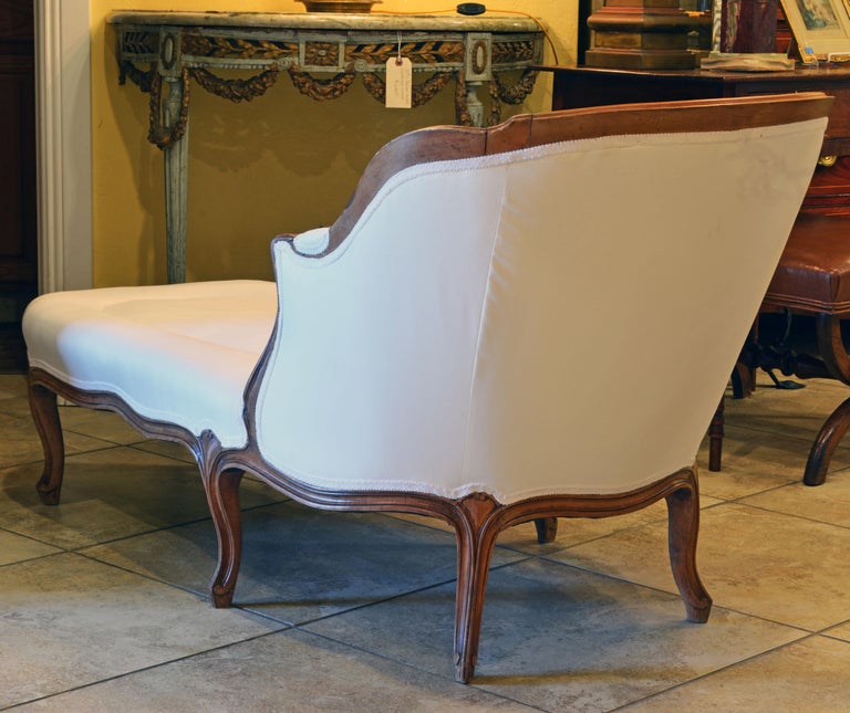 This elegant and comfortable French Provincial chaise longue features a delicately carved walnut frame resting on 6 carved cabriole legs. It has recently been reupholstered and covered with white fabric.