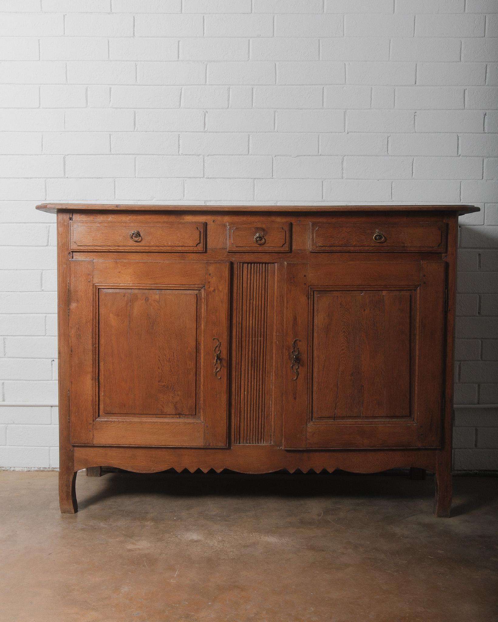 This charming 19th-century French Provincial buffet showcases the rustic elegance typical of countryside craftsmanship. Made from solid oak, it features a warm, rich patina that enhances its natural beauty. The piece includes three drawers above two