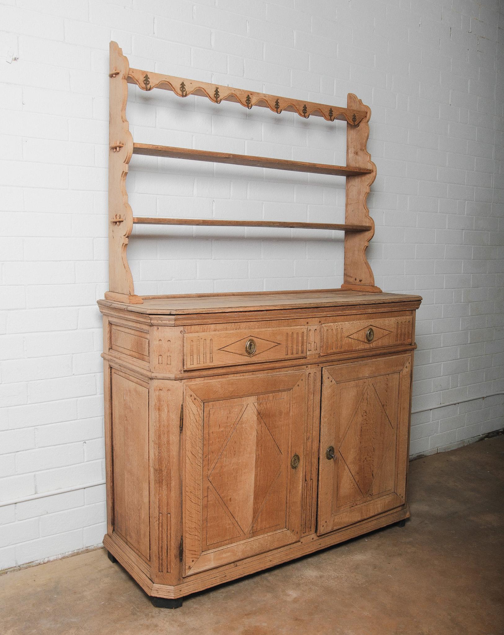A charming 19th century French Provincial oak dresser with a beautifully aged patina and practical plate rack top. This two-part piece features a lower cabinet with two paneled doors and two drawers, adorned with original brass escutcheons and