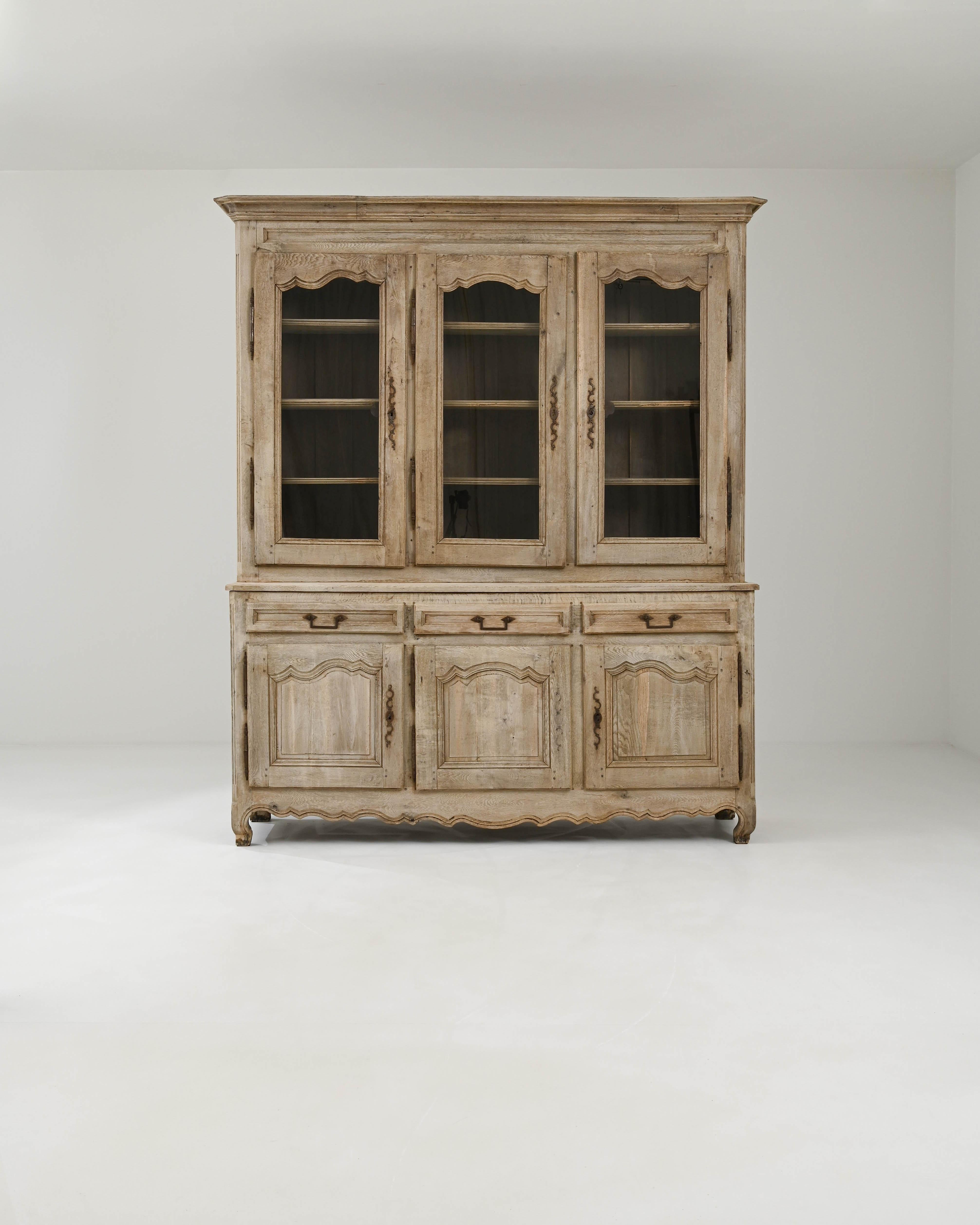 This antique oak vitrine would have originally been used to display the prized chinaware of a Provincial household. Built in France in the 1800s, the three windows of the upper cabinet give a view onto an array of shelves, gracefully accented by the