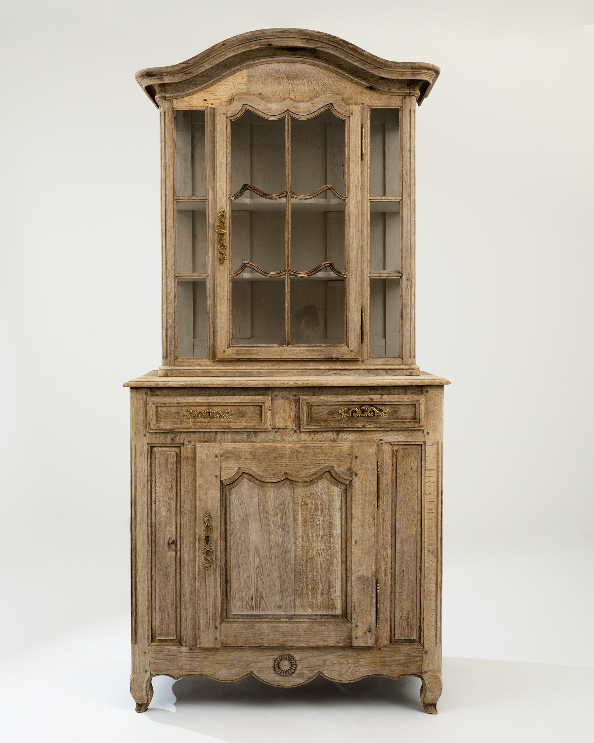 A graceful design in natural oak gives this antique French Provincial vitrine a timeless charm. Hand-crafted in the 1800s, elegant mullions mirror the flowing shape of the paneling on the doors of the upper window and lower cupboard to create a