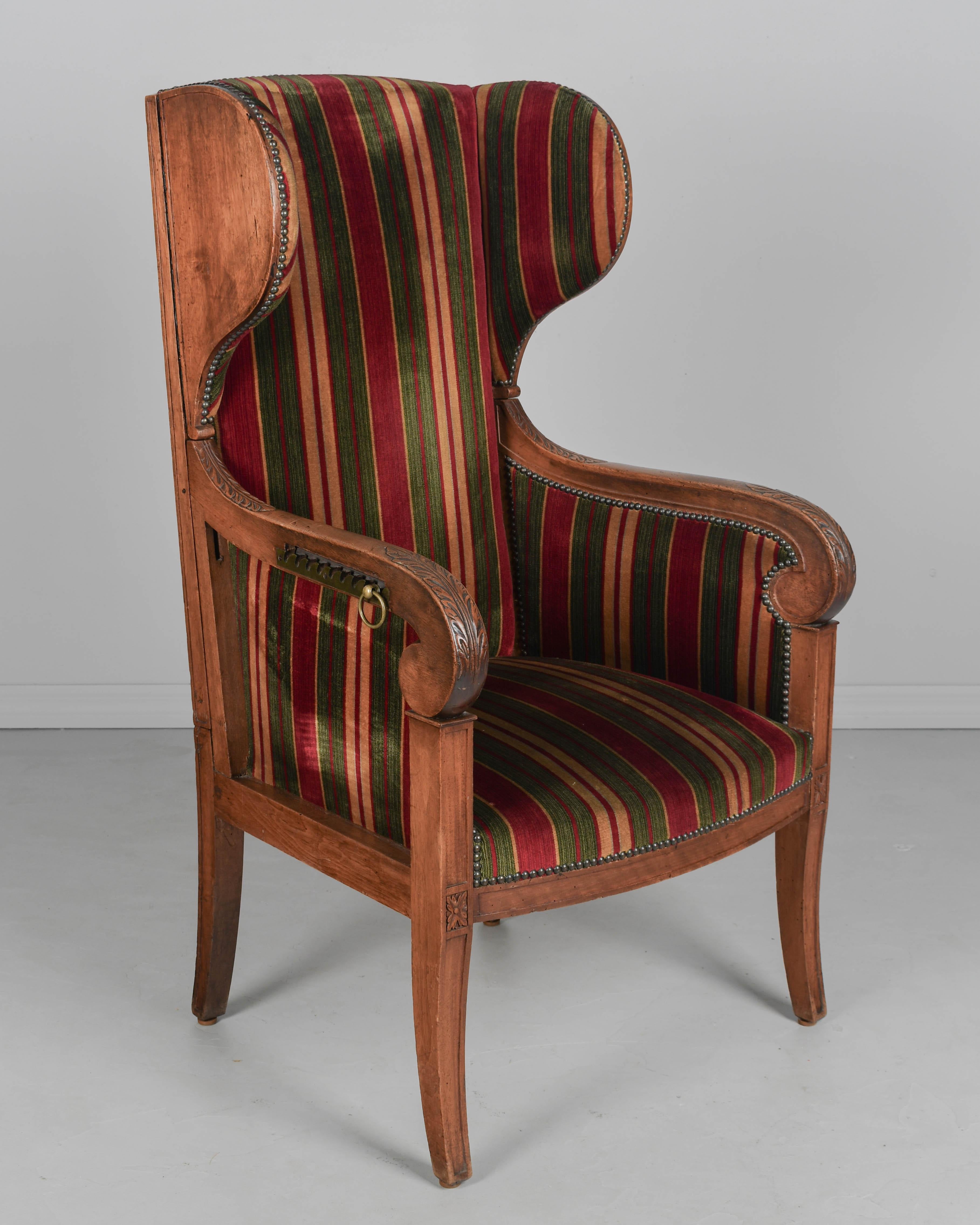 Ein gepolsterter Ohrensessel im französischen Louis-Philippe-Stil aus dem 19. Die Neigung der Rückenlehne lässt sich über einen Messingring und Sägezahnmechanismen an den Seiten der Arme einstellen. Massiver Nussbaumrahmen mit geschnitzten Details