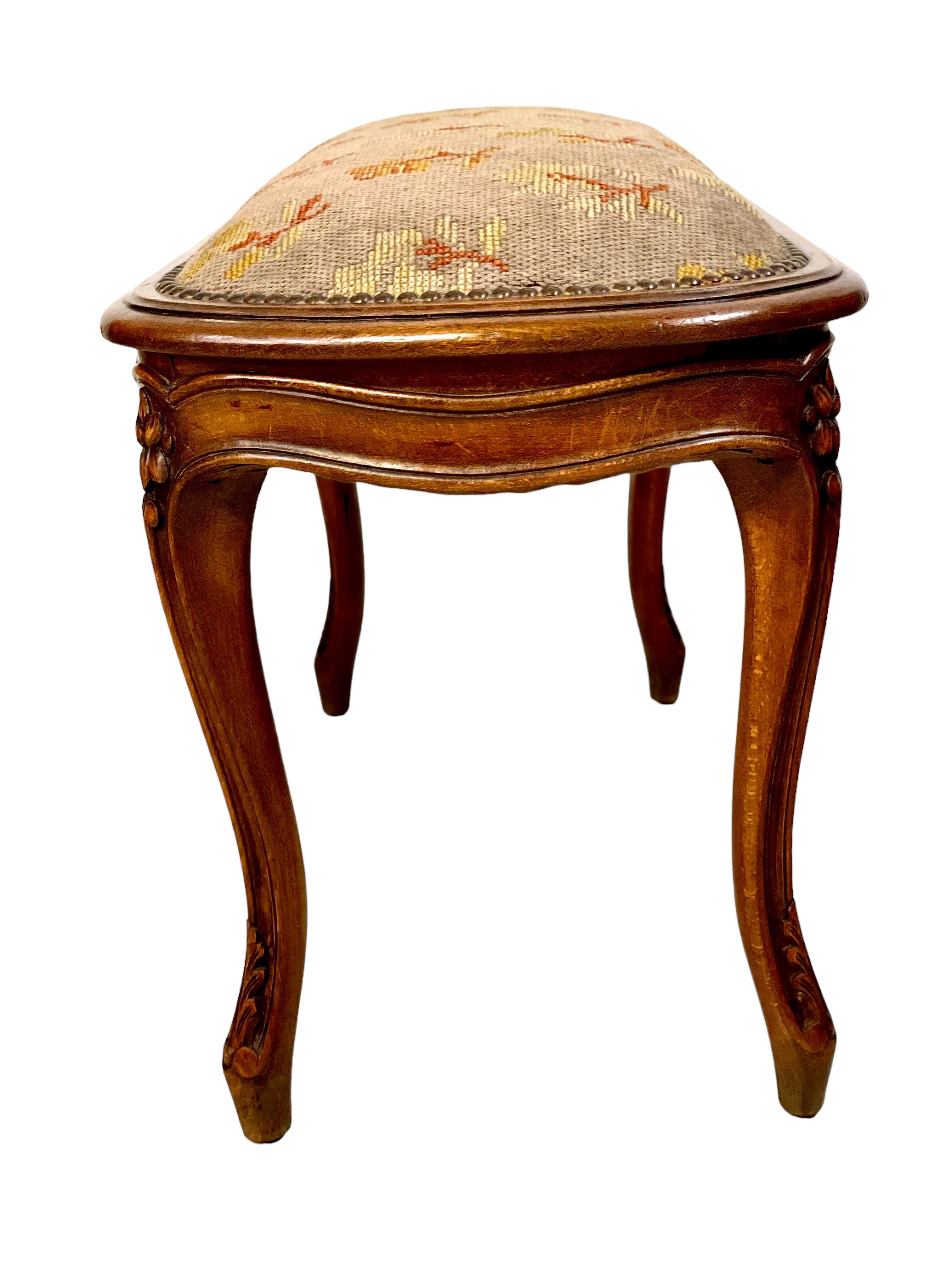 A very pretty 19th century Régence style piano stool in polished walnut, its padded cushion upholstered in a delicate needlepoint tapestry featuring a design of rosebuds and leaf sprays and secured all round with a nailhead trim. The banquette is