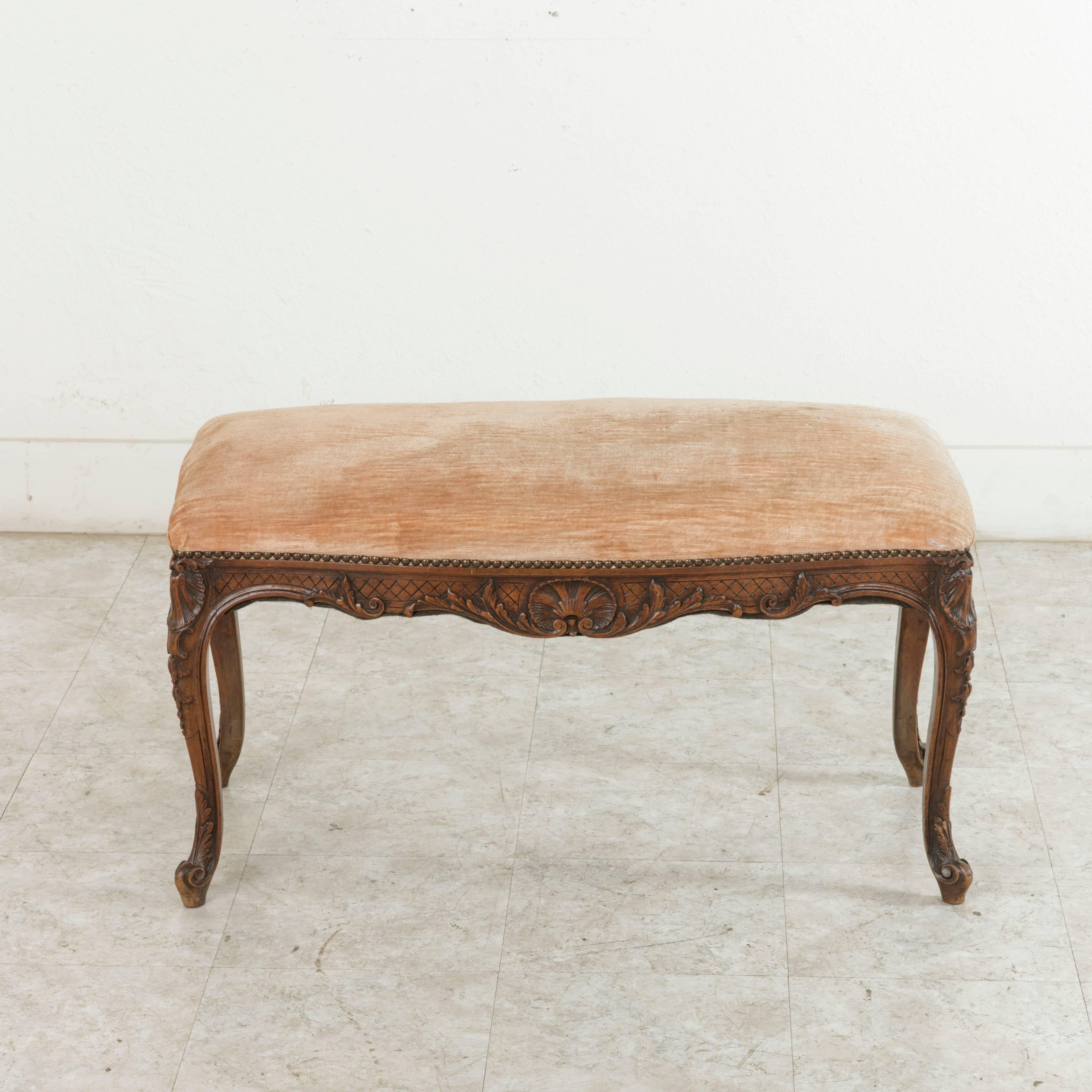 This late 19th French Regency style piano bench or banquette features hand carvings on all sides. A diamond pattern with a central scalloped shell flanked by gadrooning leaves adorns each side. The scalloped shell motif is repeated on each corner.