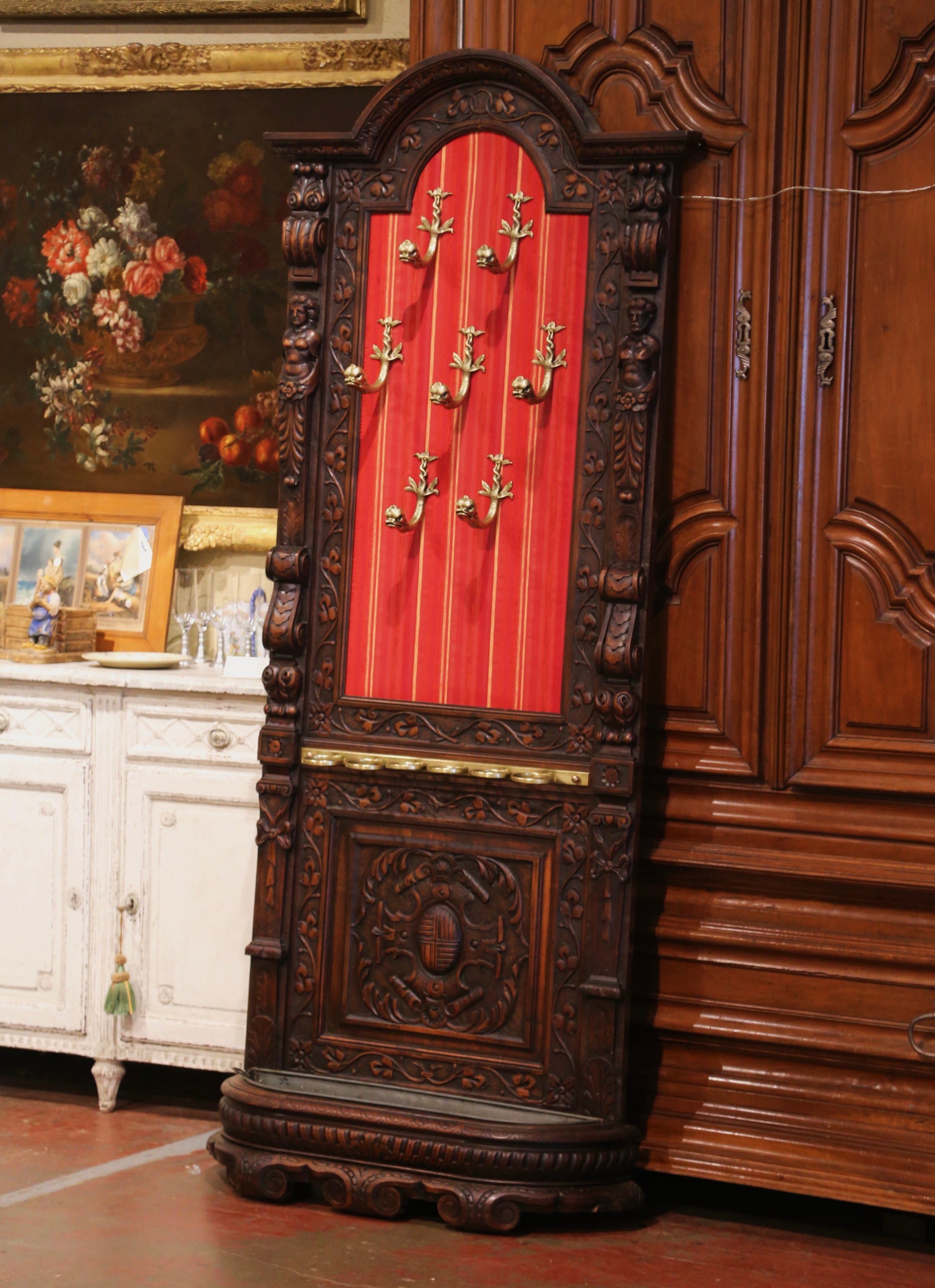 This elegant antique Gothic coat rack was crafted in southern France, circa 1880. The symmetrical stand features an arched bonnet top with molded cornice, embellished with floral motifs. The paneled backboard is accented with male and female