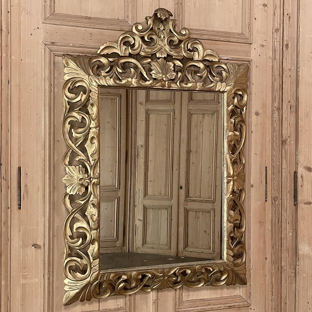 19th century French Renaissance hand-carved giltwood mirror was carved in the Italian style from solid wood, then gilded for an opulent effect. The entire frame consists of shell, foliate and scrollwork motifs with fleurs de lys designs on each
