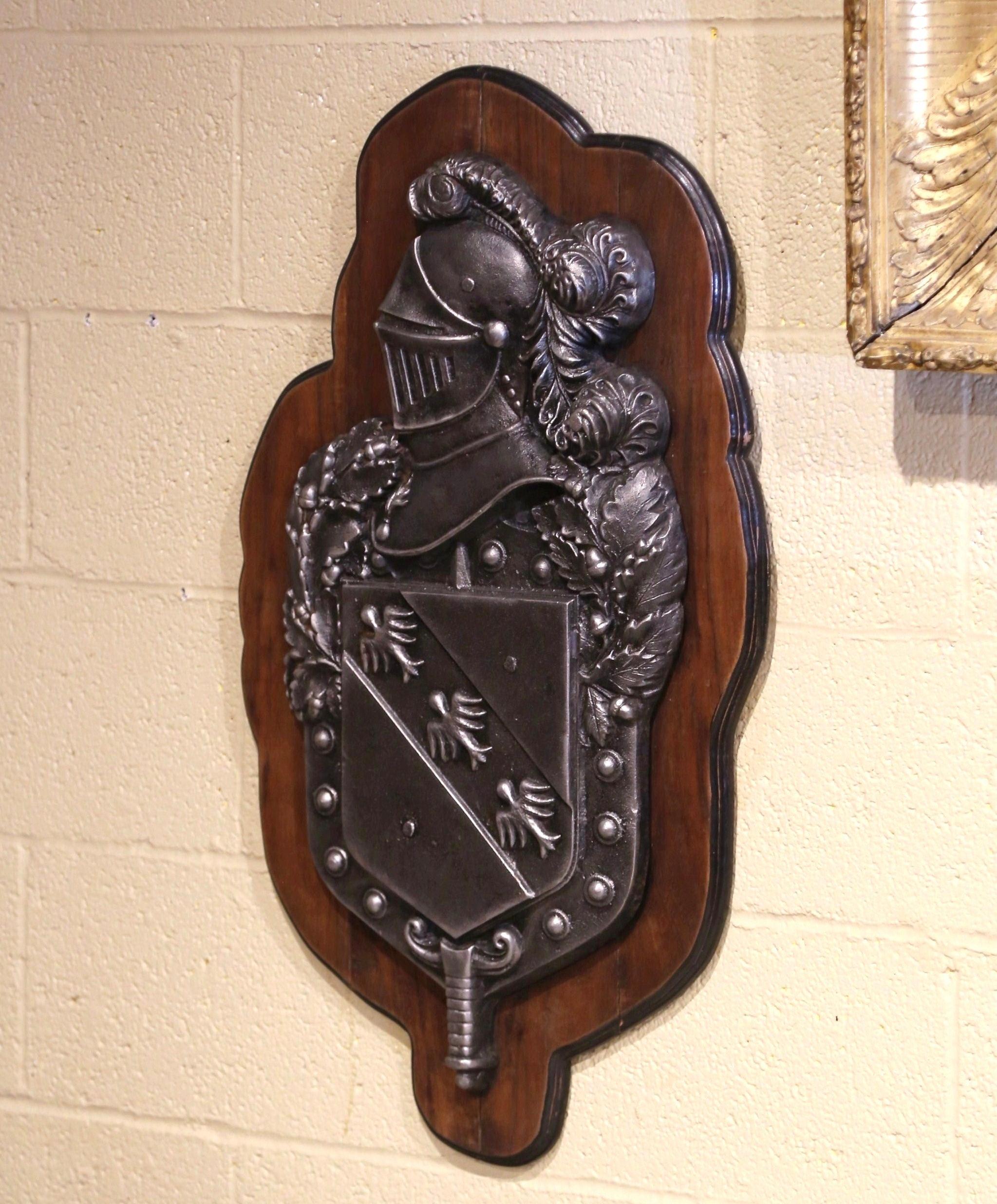 Decora uno studio o un ufficio maschile con questa elegante targa antica. Realizzata in Francia intorno al 1880, la decorazione da parete presenta uno stemma con un'armatura da cavaliere reale medievale con piuma su uno stemma di famiglia con