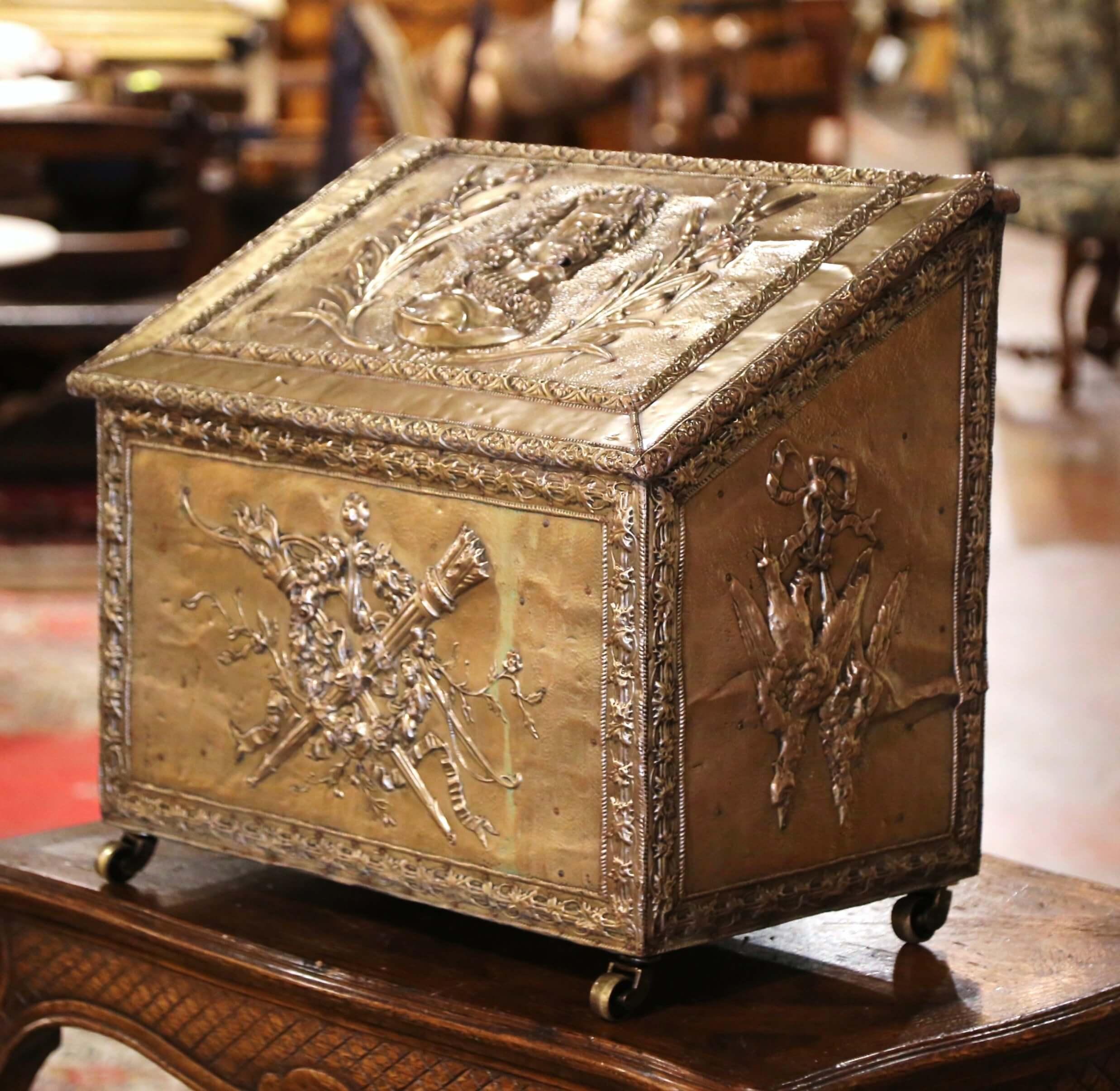 Crafted in France, circa 1870, the antique brass coffer is mounted on a wooden frame, and stands on caster wheels. The slant top opens up with stopping chain revealing inside storage. The large coal bin is decorated with repousse hunting motifs on