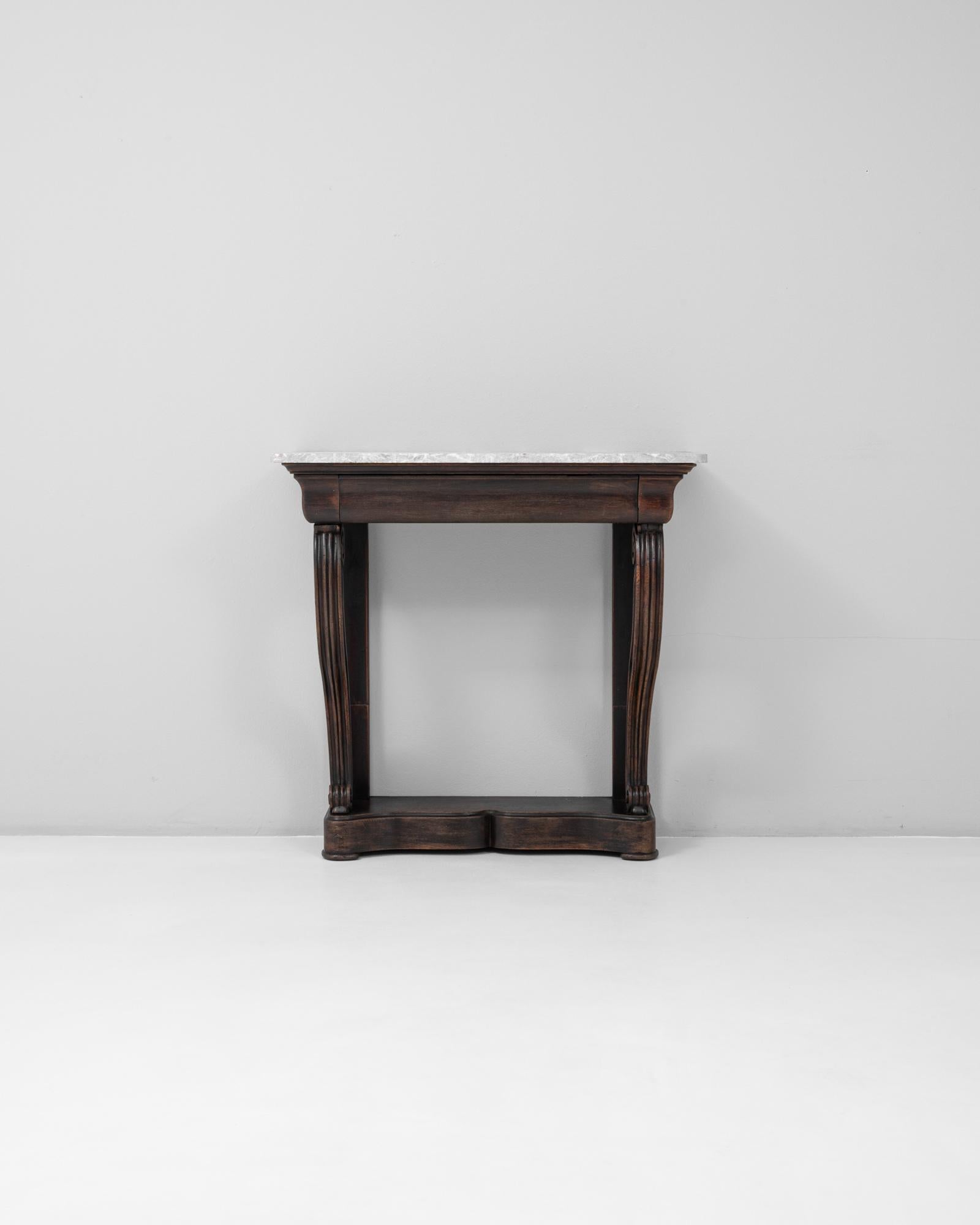 This 19th Century French Restauration console table with marble top and original patina presents a refined yet quietly dramatic silhouette characteristic of the period. The piece features a shaped white marble top with soft veining, resting on a
