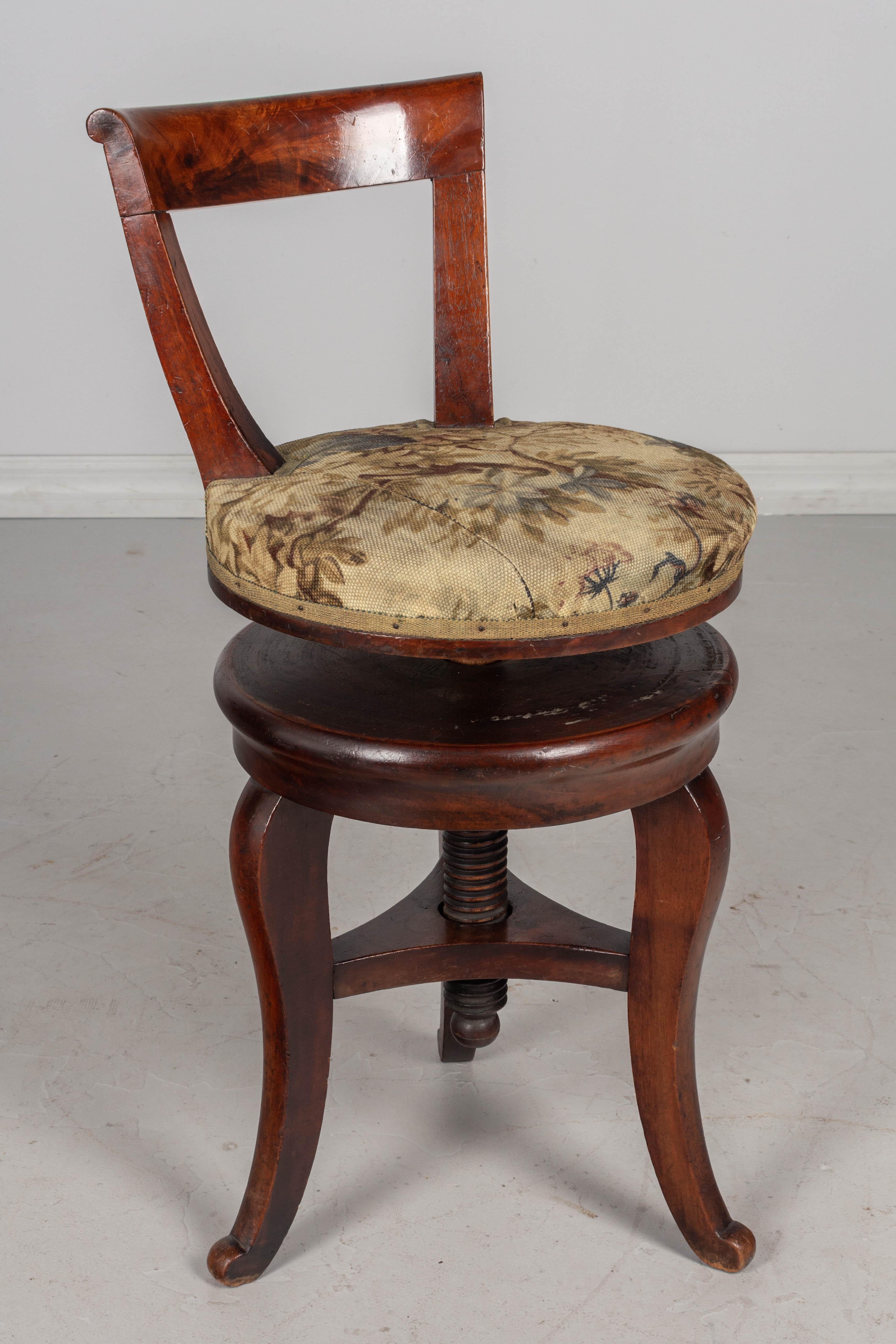 A 19th century French Restauration style circular three leg swivel stool made of solid mahogany with large turned wood center vice. This small chair was made for a harpist and the height may be easily adjusted for the comfort of the musician.