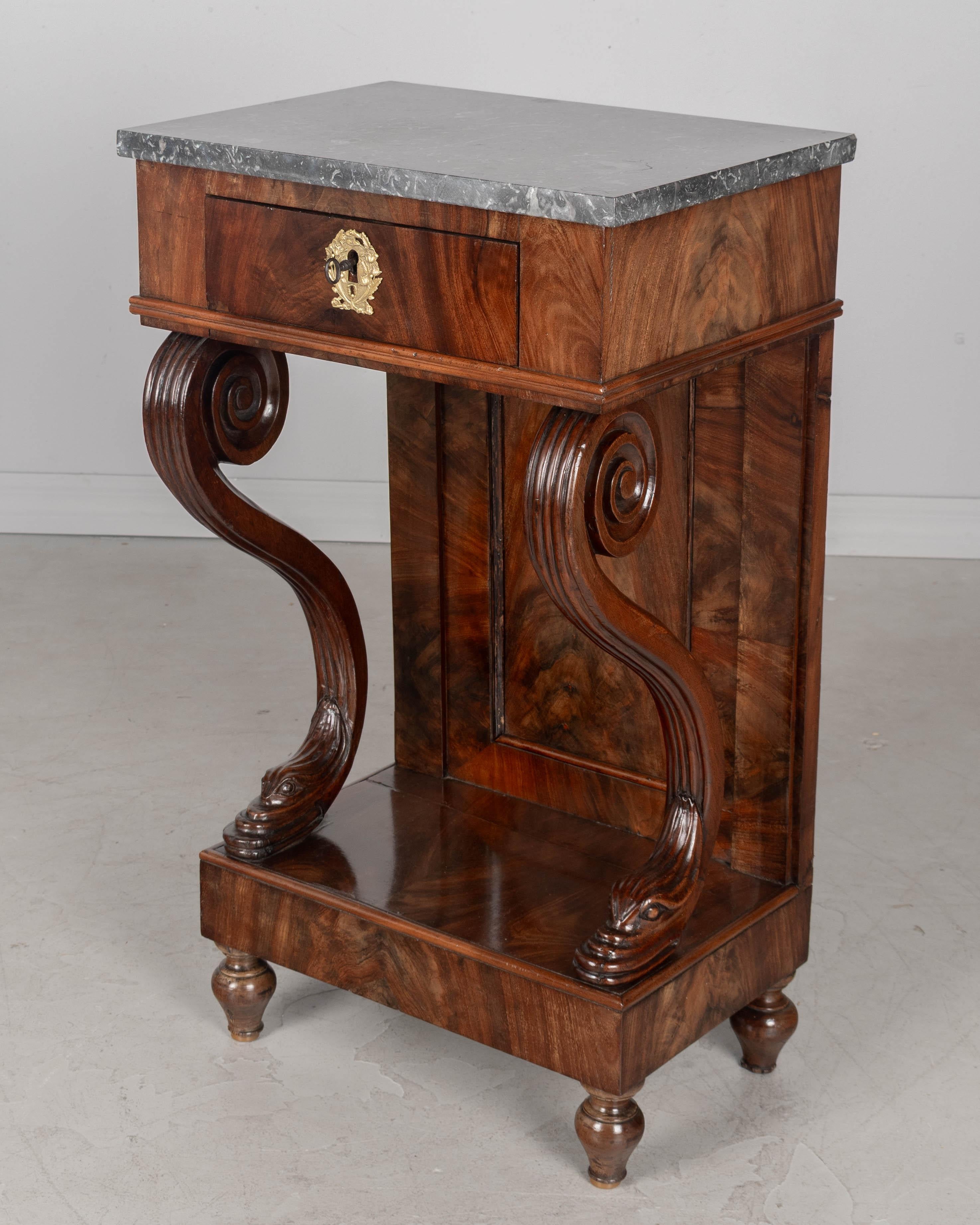 Tavolino o piccola console in mogano del periodo della Restaurazione francese del XIX secolo. Cassetto a coda di rondine con rosetta decorativa in ottone, serratura funzionante e chiave. Supporti curvi in mogano massiccio con teste di delfino