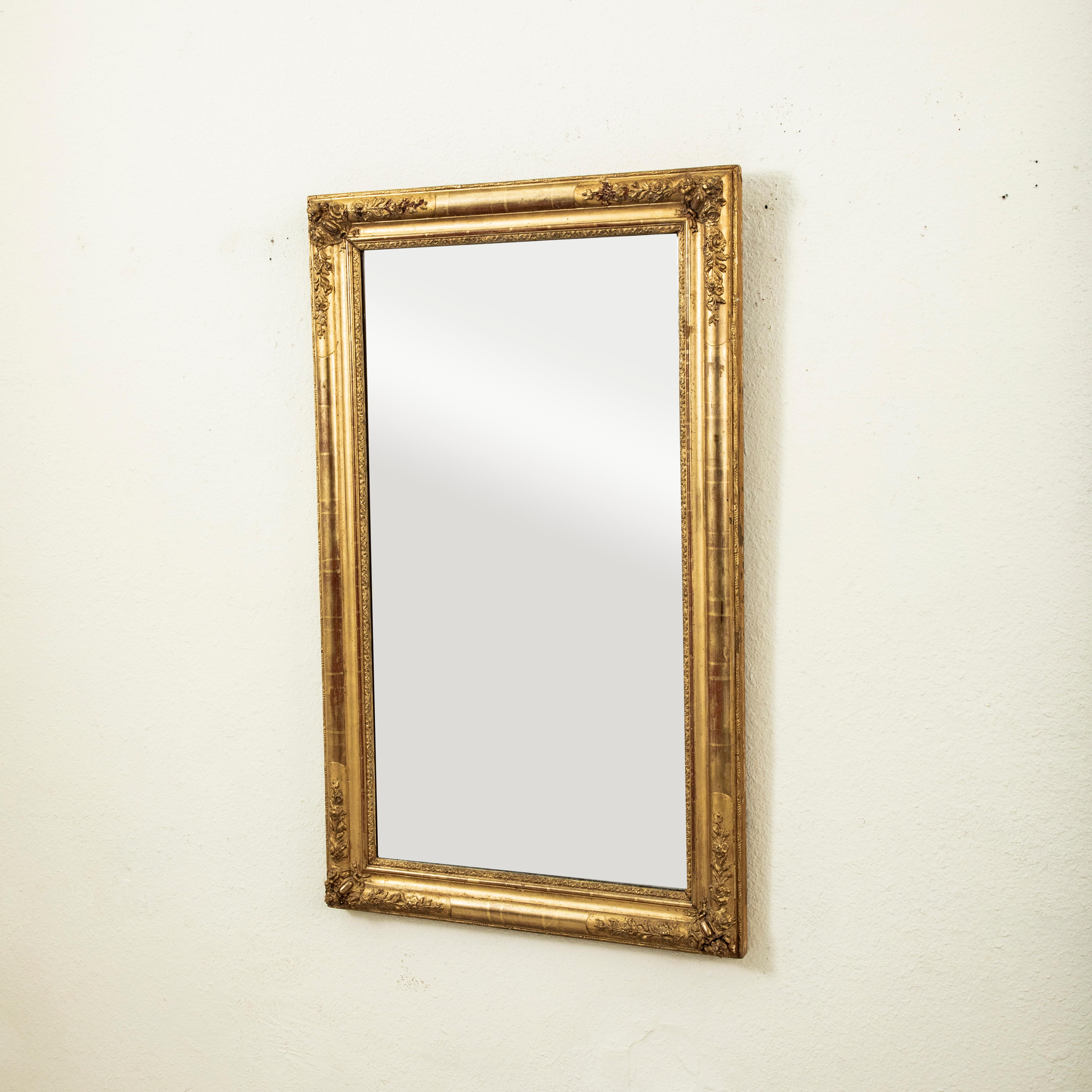 Ce miroir en bois doré d'époque Restauration française du début du XIXe siècle est doté d'un verre au mercure d'origine. Le cadre est orné de cartouches floraux dans chaque coin, ainsi que d'autres détails floraux, et une bordure de volutes entoure