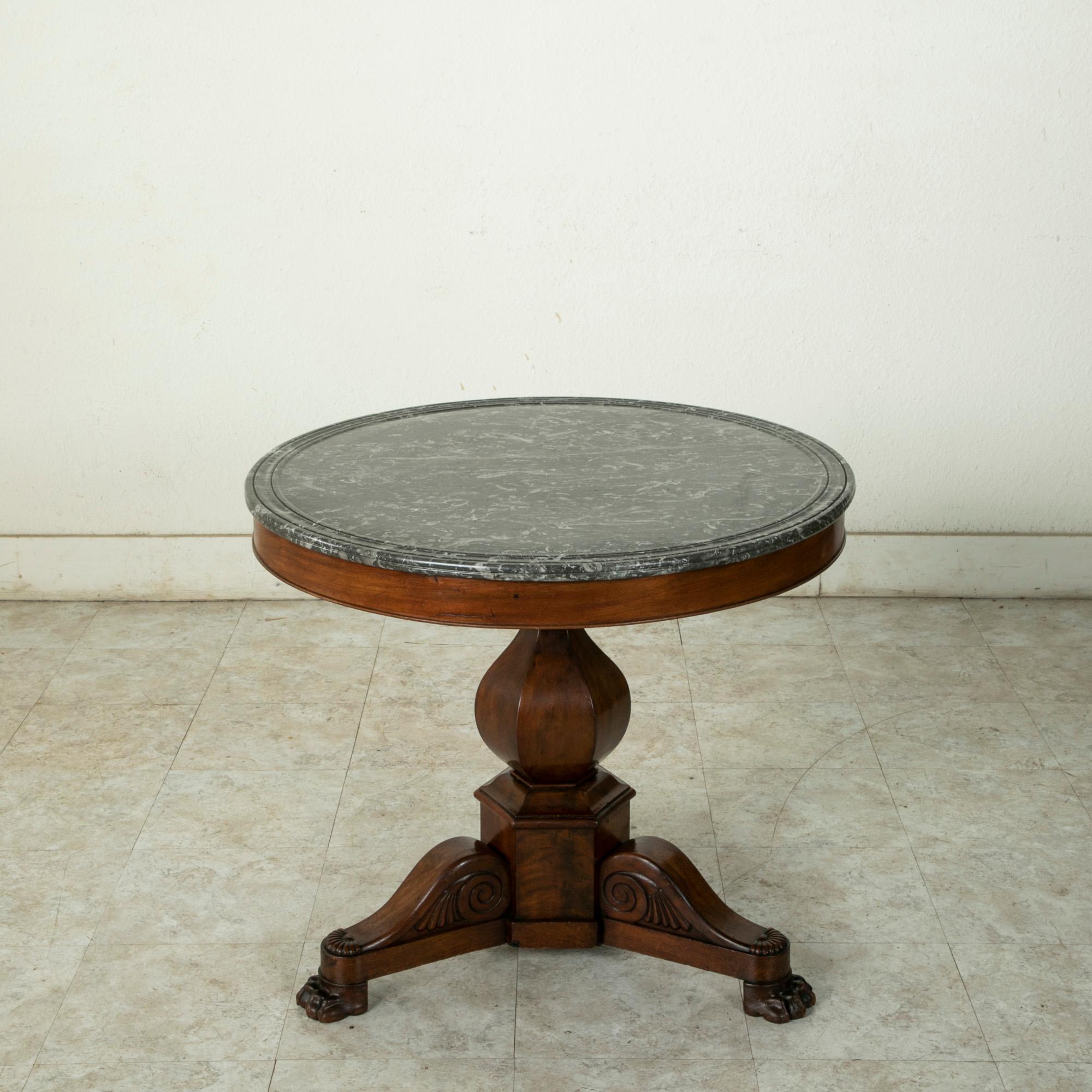 This early nineteenth century Restauration period mahogany gueridon or pedestal table features a multi-beveled Saint Anne marble top. Its 31.75 inch diameter top is supported by a faceted central pillar that rests on a tripod base. Its three legs