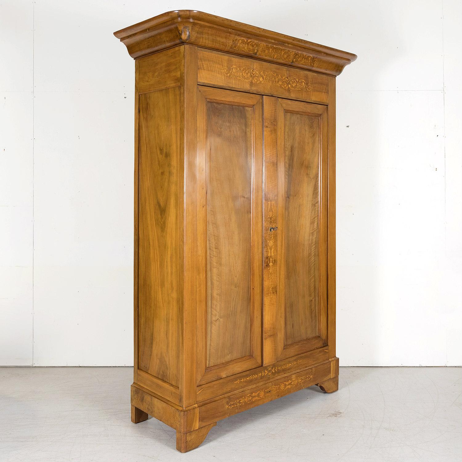 An impressive French Restauration period armoire, circa 1825, handcrafted of solid walnut accented with rich fruitwood marquetry inlay by talented artisans in Lyon, the capital city in France’s Auvergne-Rhône-Alpes region, world renowned for its