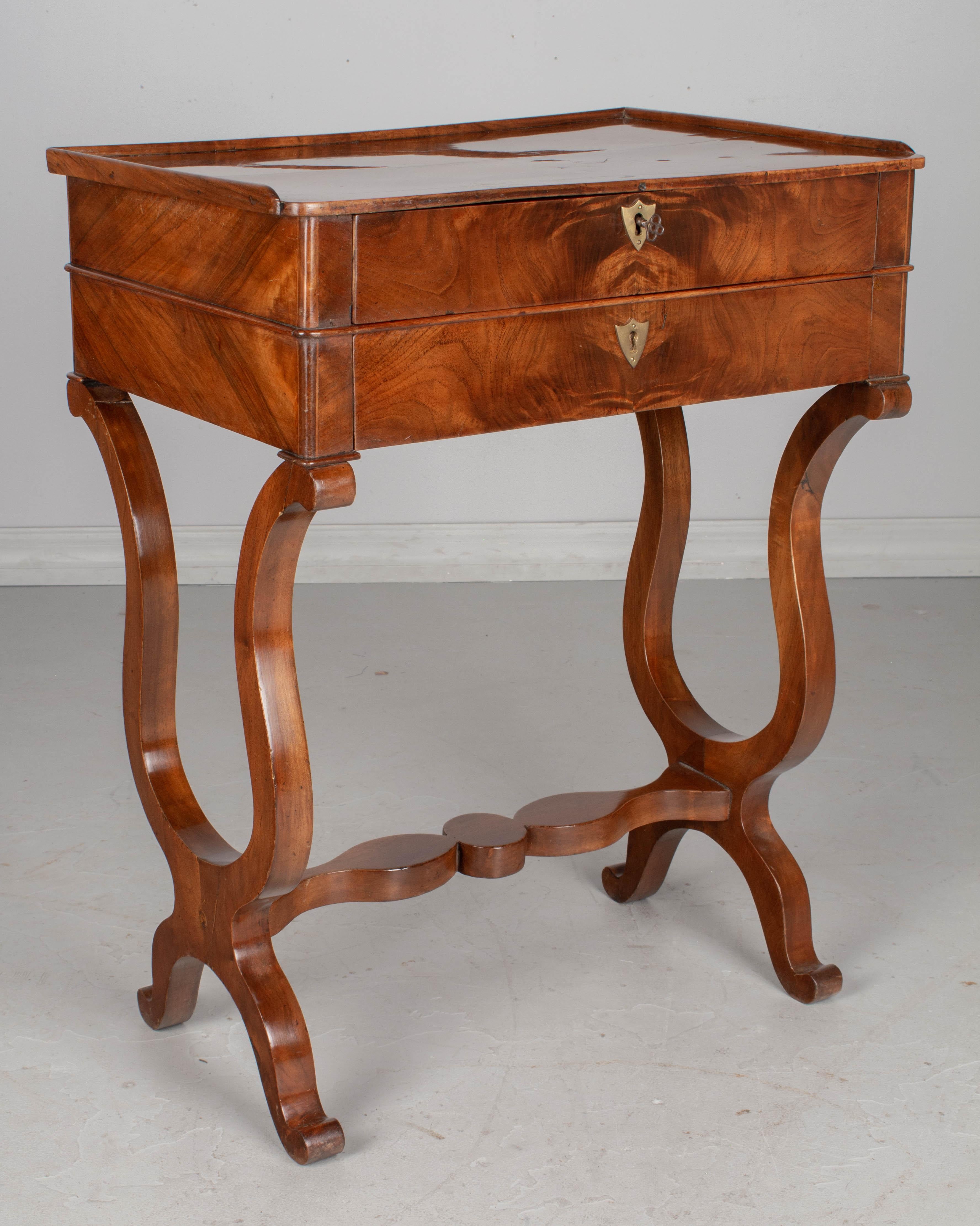 A 19th century French Restauration style side table made of book matched veneer of walnut with beautiful wood grain and French polish finish. Two dovetailed drawers with working locks and one key. Replaced brass escutcheons. A sturdy table with lyre