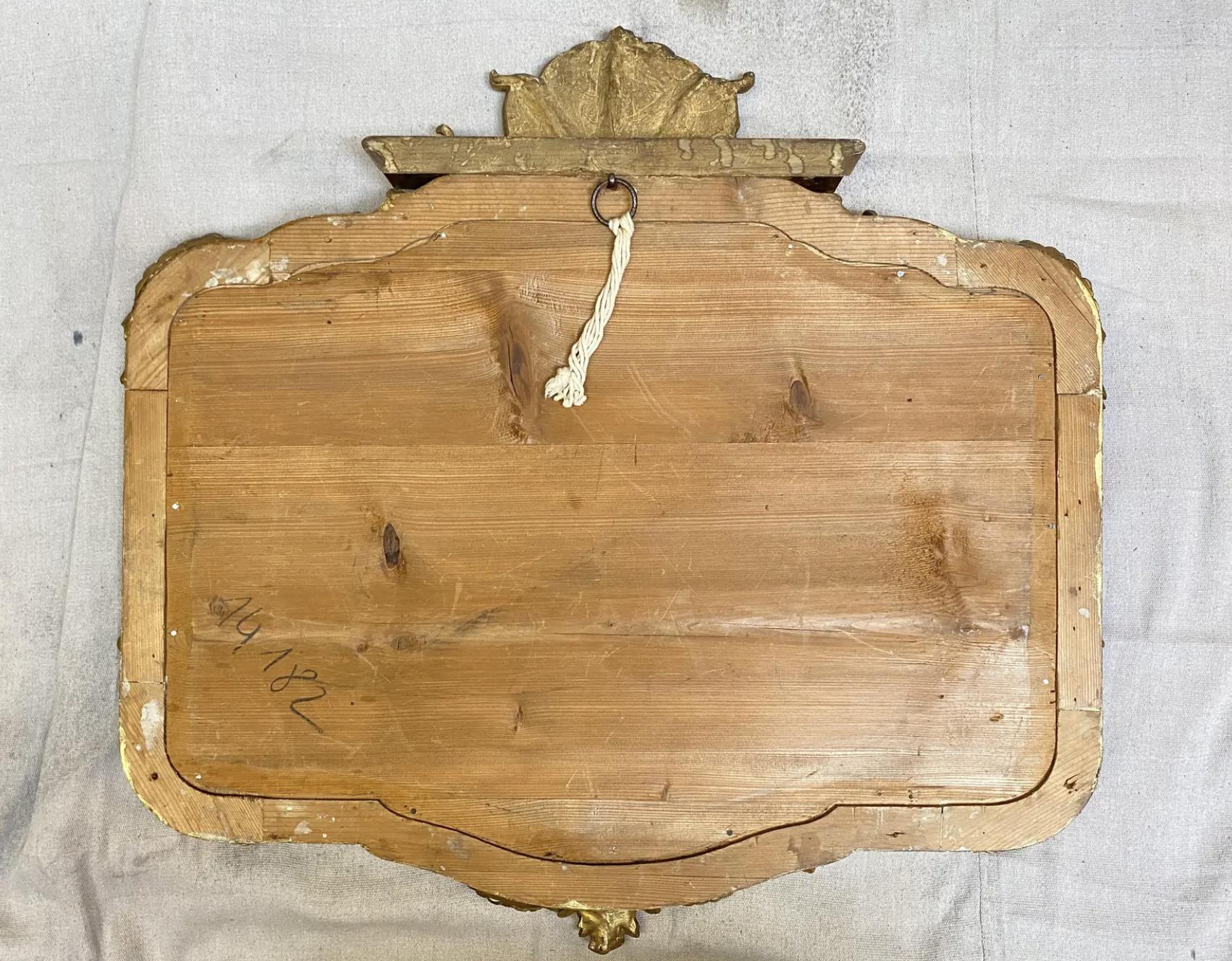 Miroir rococo français en bois doré du milieu du XIXe siècle. Cadre en pin sculpté à la main, rehaussé de gesso, avec une crête et des reliefs courbés autour du miroir d'origine biseauté à la main d'un pouce.