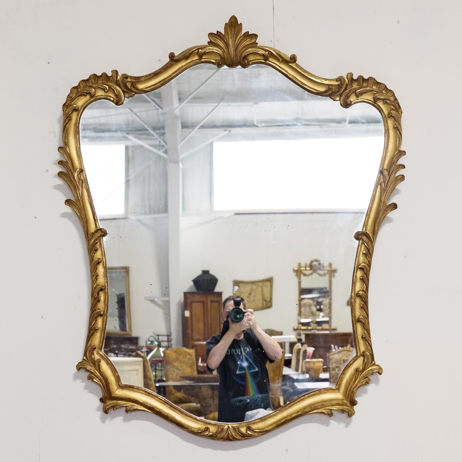 Impressive 19th century French Rococo Louis XV style hand carved giltwood mirror having its original glass, circa 1850s. The shapely frame features hand carved acanthus leaves and scroll motifs with red oxidation showing through the beautiful water