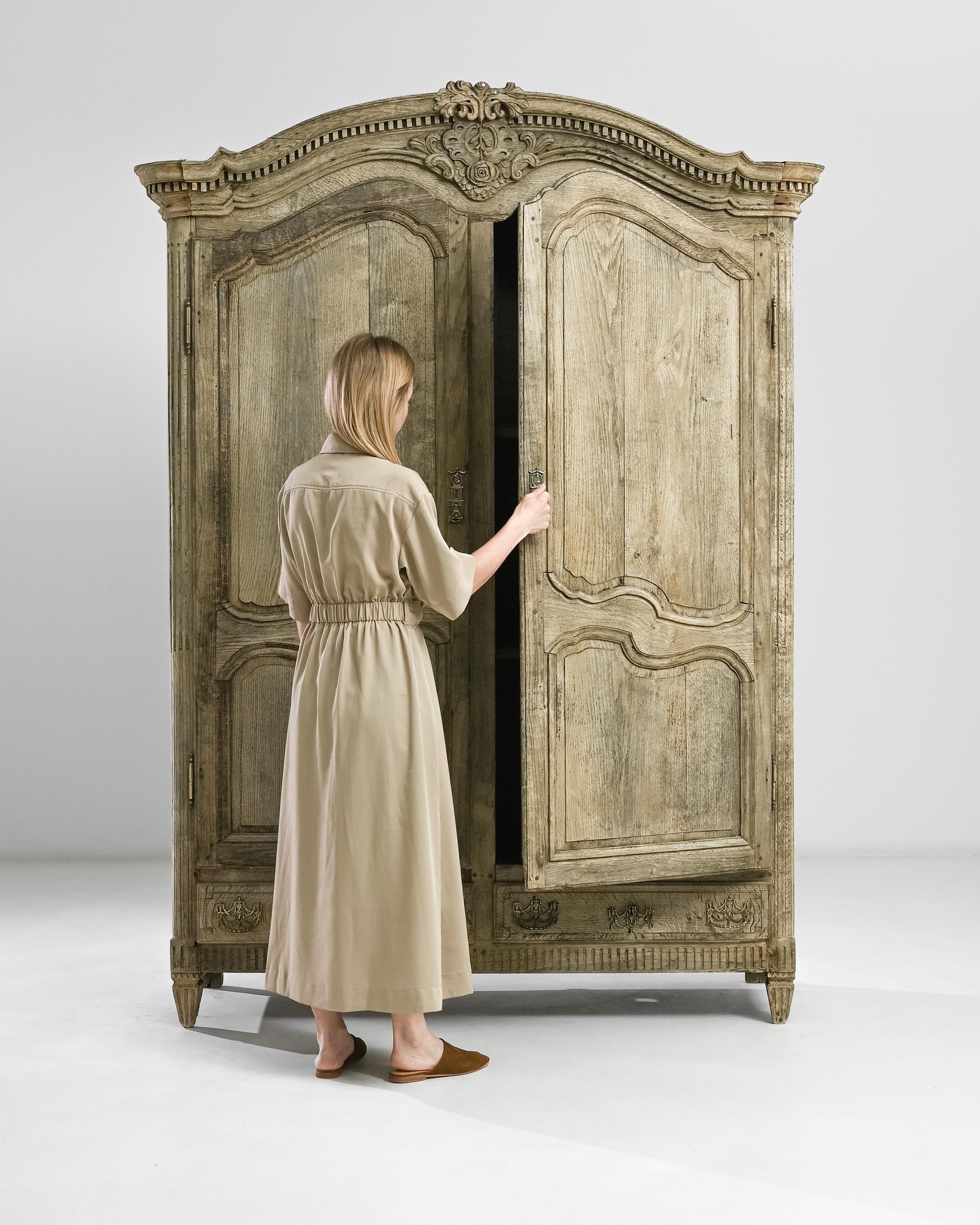 This elegant 19th century armoire is alive with refined French Rococo elements. The central molding flaunts a masterfully carved rosette surrounded by decorative fish scales, rich foliage and scrolls reminiscent of sea waves. The door locks