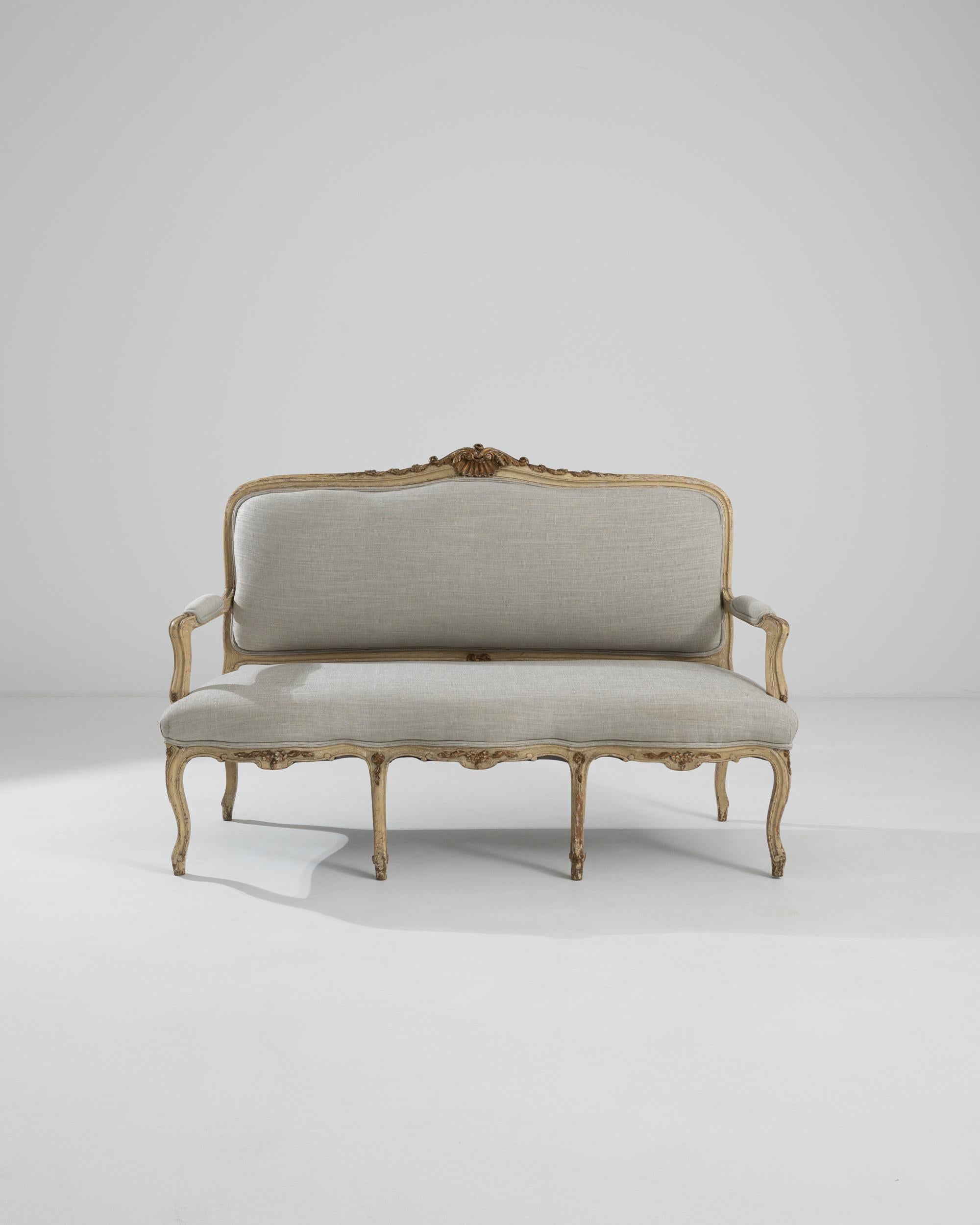 Elegant and refined, this antique wooden settee is a Rococo gem. Made in France in the 1800s, this piece would have originally been used for entertaining; the light, graceful form and comfortable cushioned seat provide the perfect accompaniment to